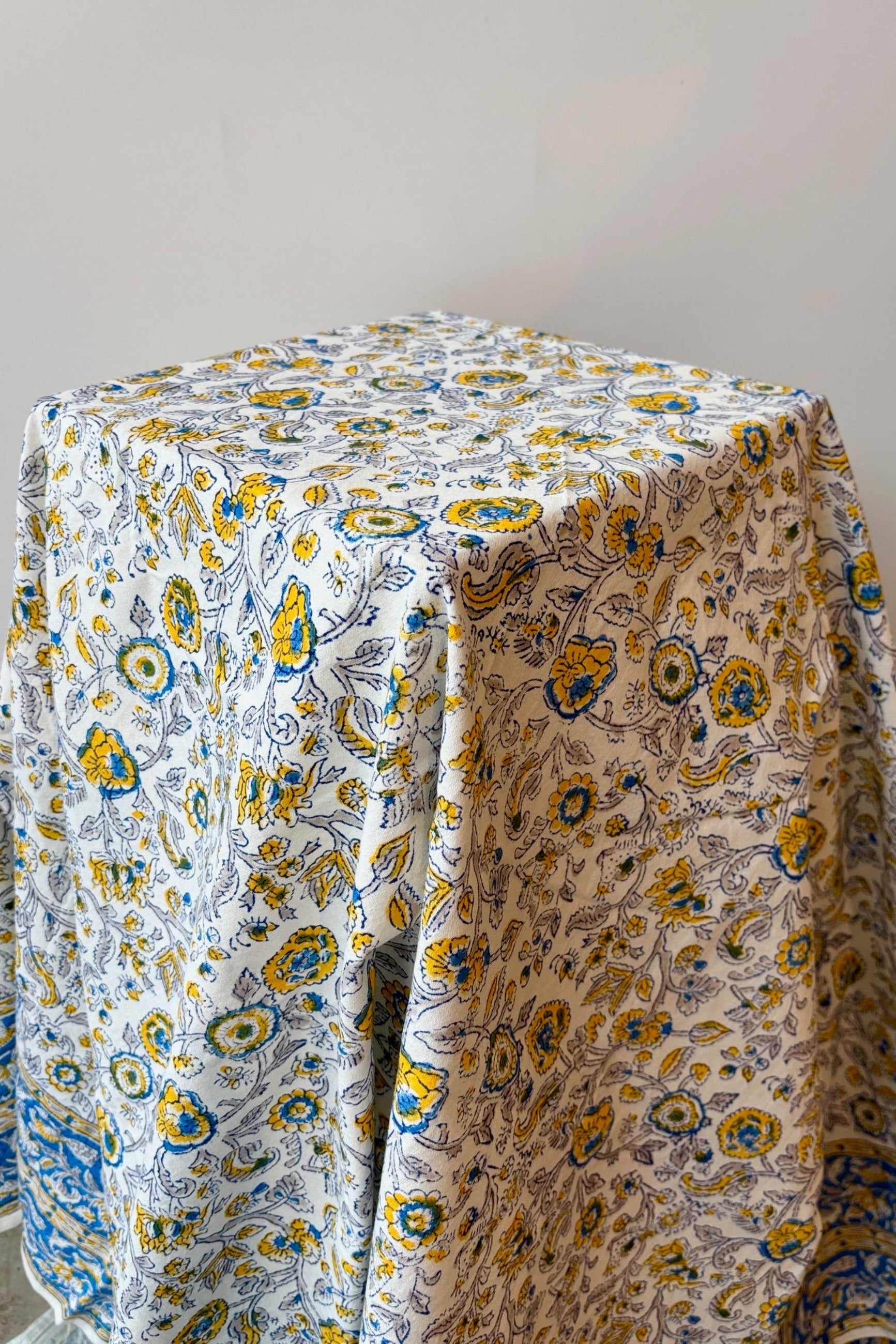 100% cotton hand block printed Provence tablecloth with blue and yellow floral motif draped over a small table ©Sprout Home