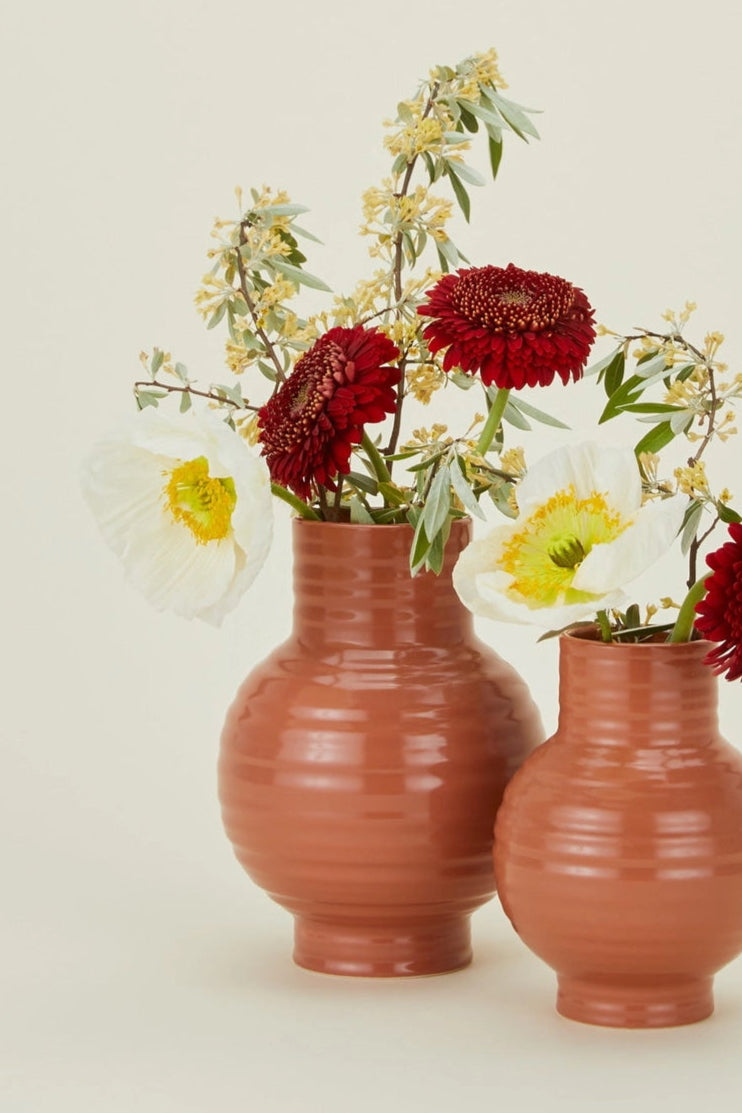 Terracotta-colored Hawkins New York Essential vases with flowers in them, on a beige background ©Hawkins New York