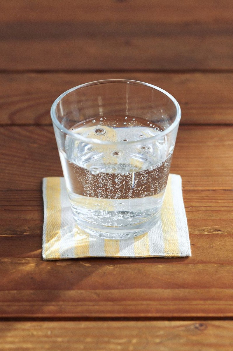 Henry Linen coaster by Fog Linen Work sitting on a wood table and a glass with water on top