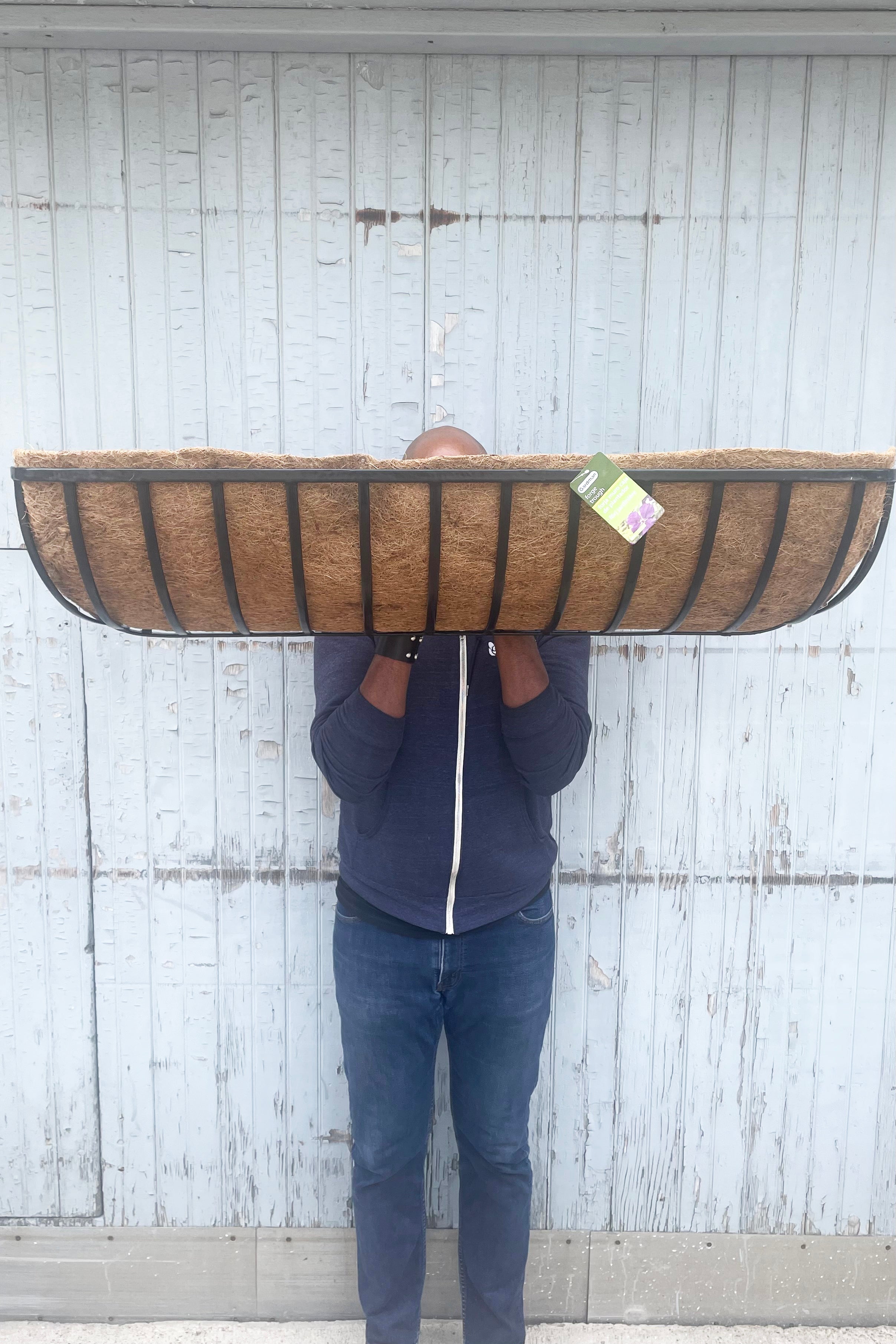 The Forge Wall Trough with Coco Liner 48" is held against wooden backdrop