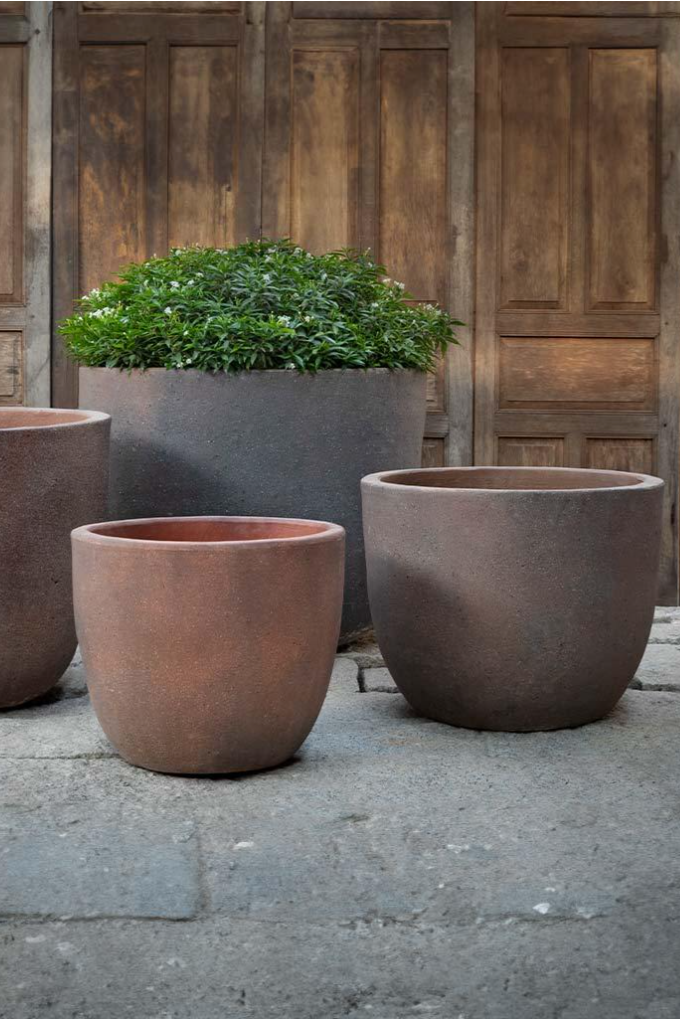 A set of four sandblasted terracotta Saba Planters in front of a wooden wall. The second largest side is half visible from the left side of the photo. All other planters are in full view from the side.