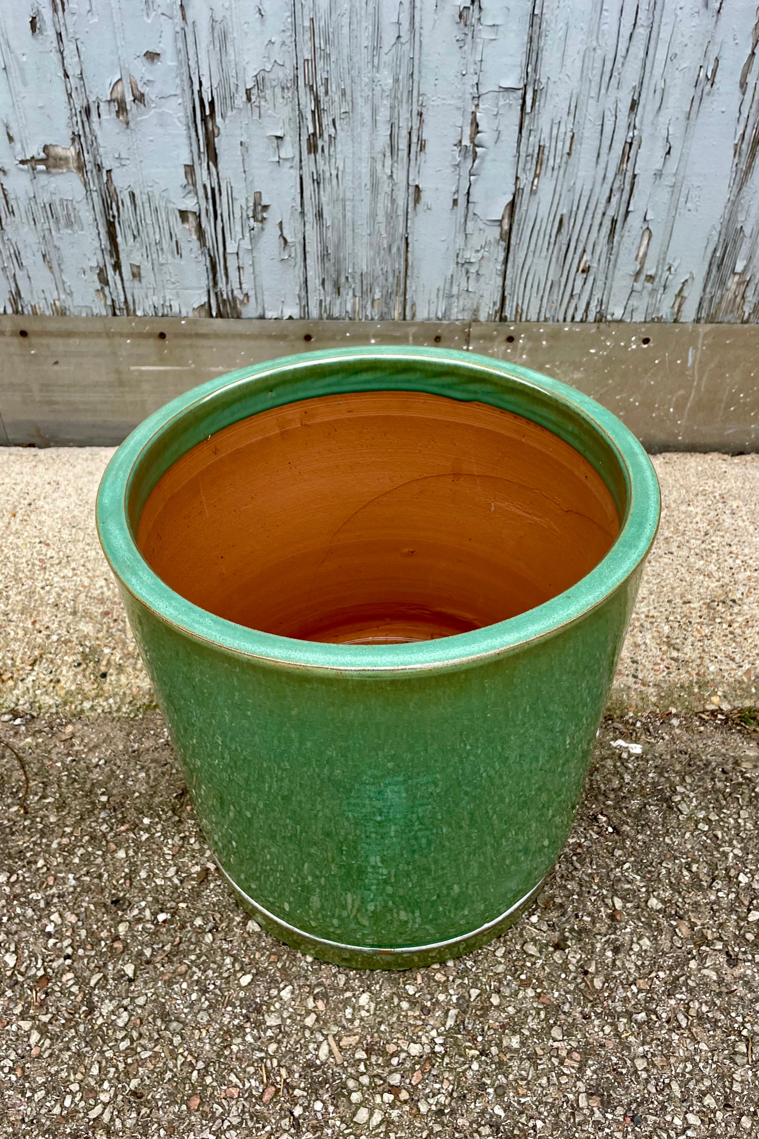 View from above. The Sea Green I/O Planter Large looking from the side at Sprout-home. The cylindrical planter sits atop a fitted saucer and is shown against a gray wall on a cement floor. The glaze is semi gloss.