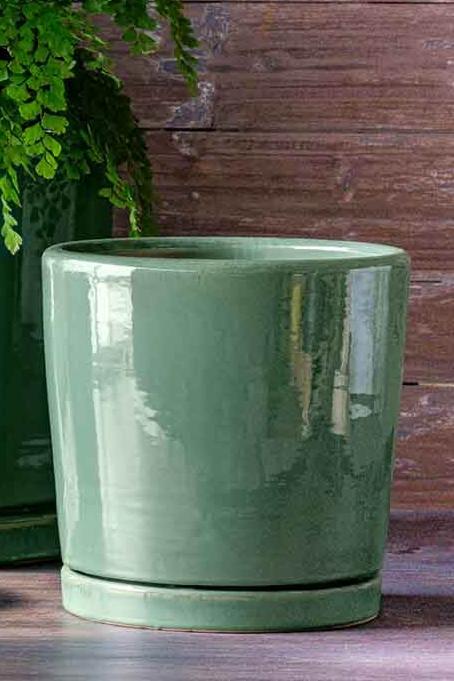 Glazed sea green i/o 2 cylinder pot and saucer against a wood wall. 
