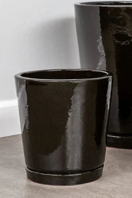 Small I/O tapered planter in a Cola brown finish on a gray floor and white wall in the background. 