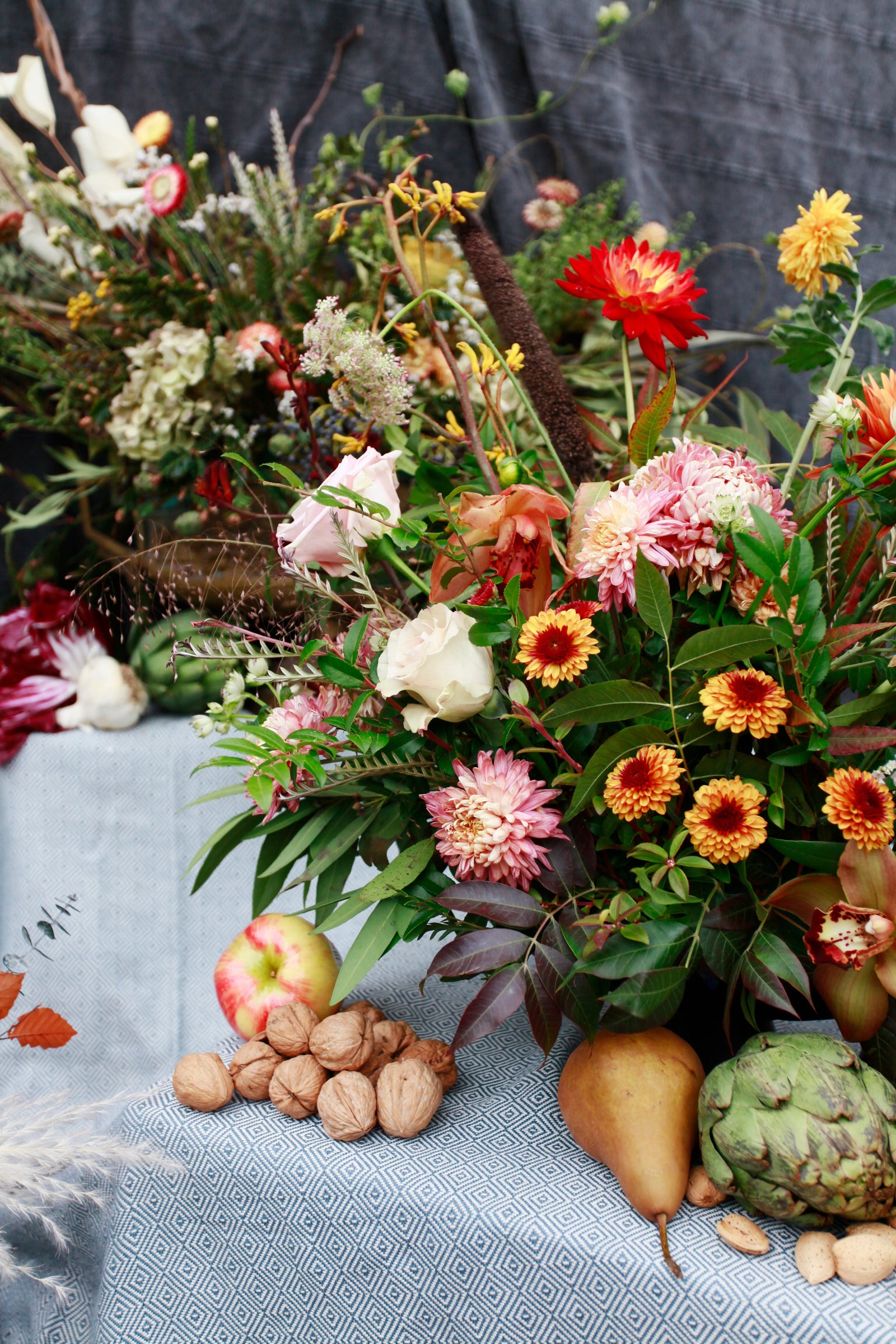 Autumnal floral arrangements and fruit created by Sprout-home in front of gray fabric. 