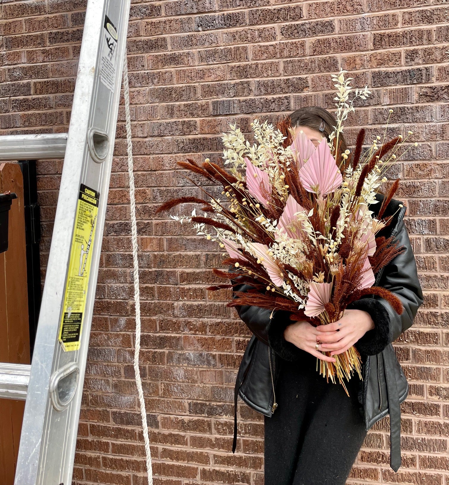 Dried floral arrangement created by Sprout-home being held by a sprout hoe employee outside the Sprout-home floral shop next to a ladder