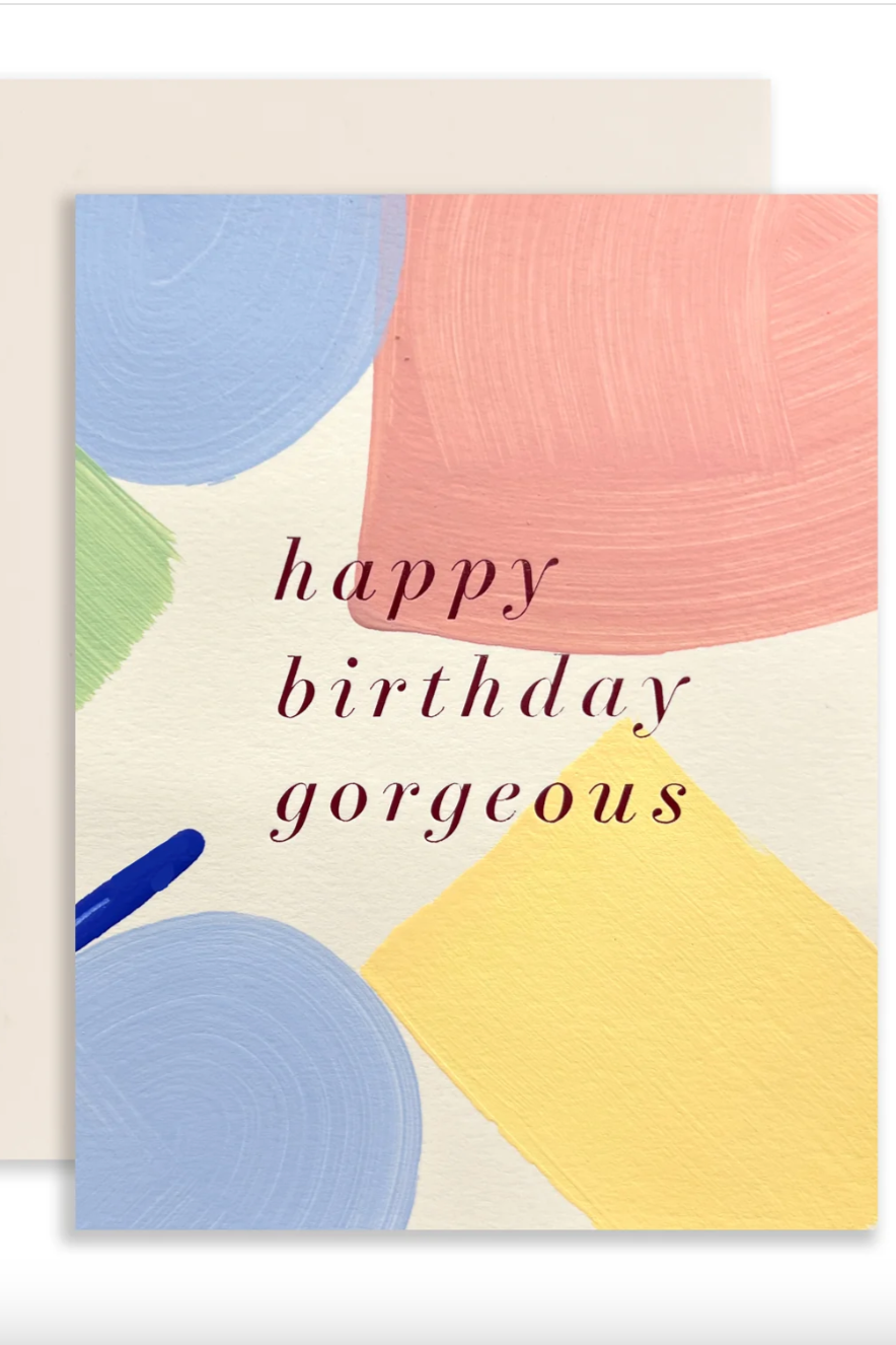 Photo of a greeting card with muted primary color paint strokes and a "happy birthday gorgeous" message printed. Shown in front of a white background ©Sprout Home