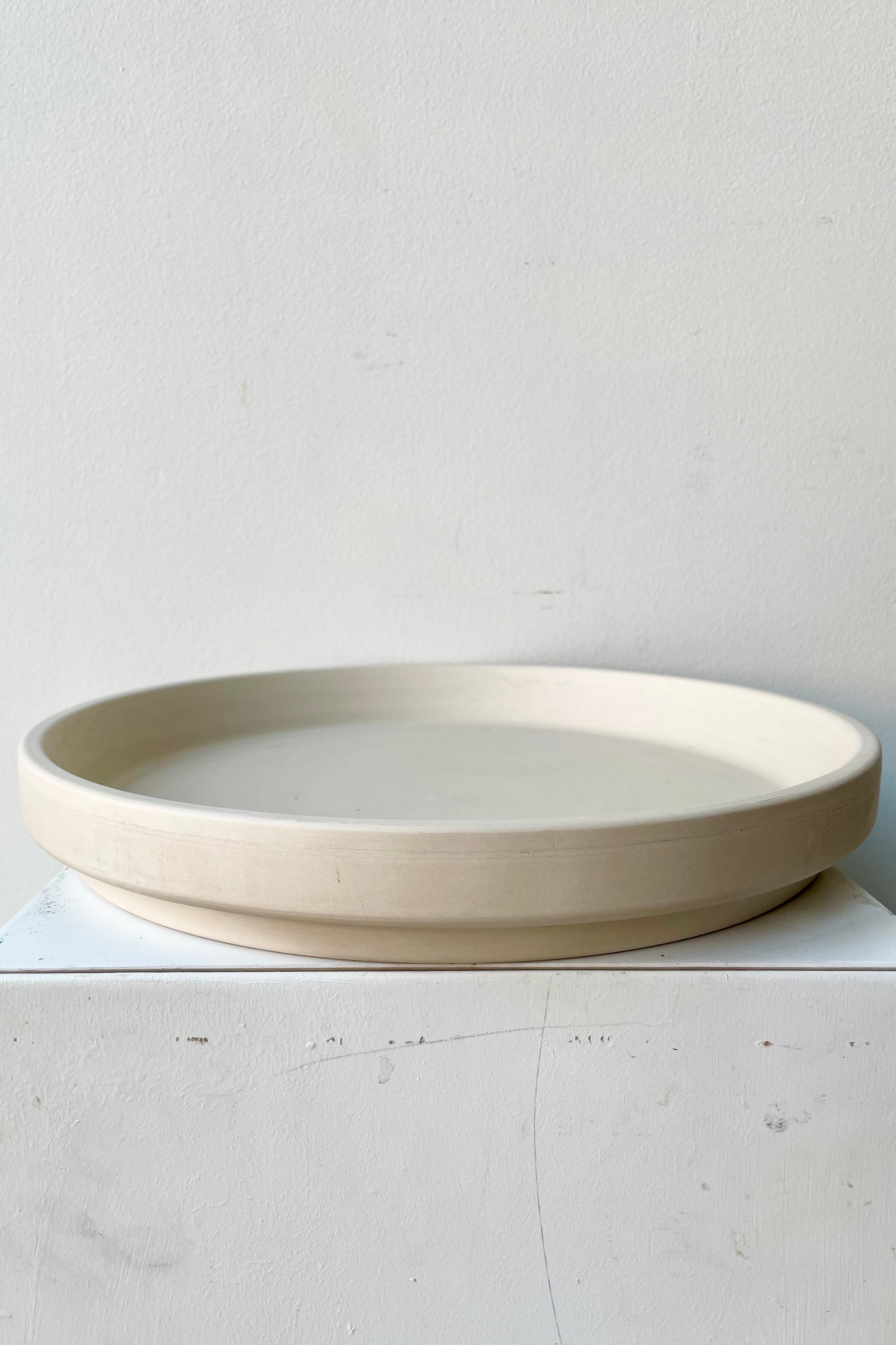 Clay Saucer granite to fit a 12" planter viewed from the side sitting on a white pedestal.