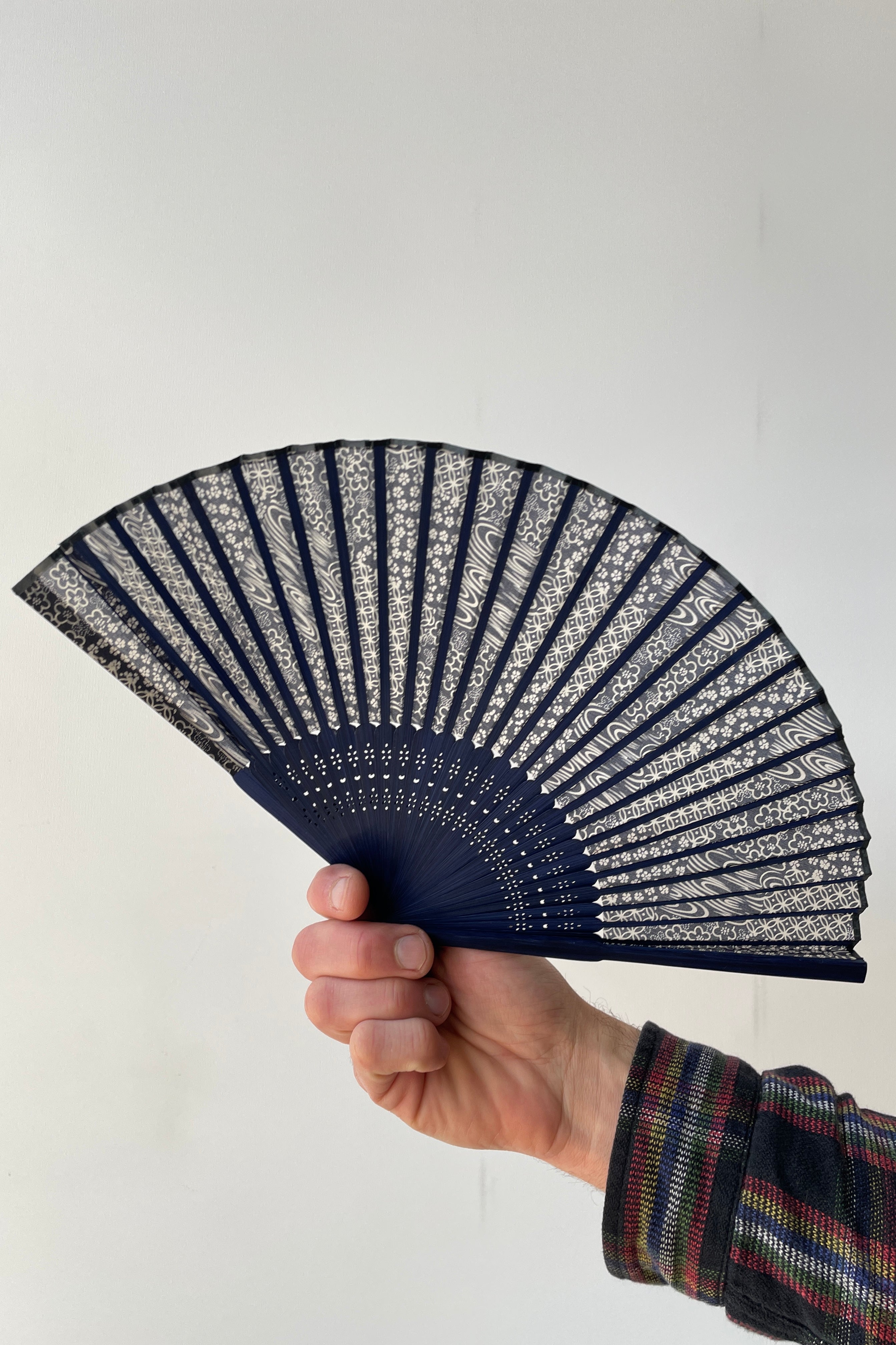 A blue swirl pattern fan with blue bamboo being held in hand against a white backdrop.  ©Sprout Home