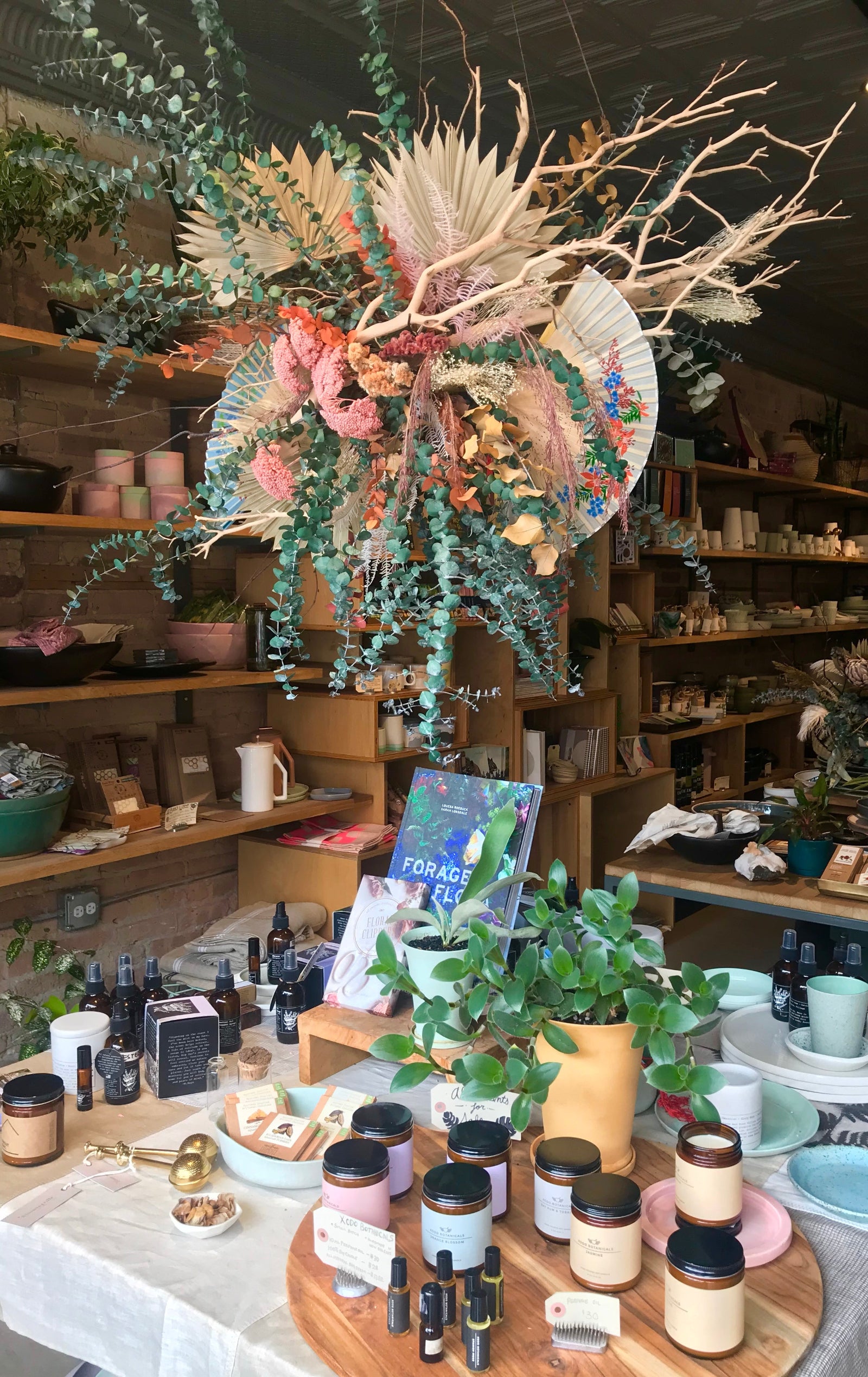 A large dried floral with fans floral display hanging above a display table with candles and shelves and homegoods in the background. 