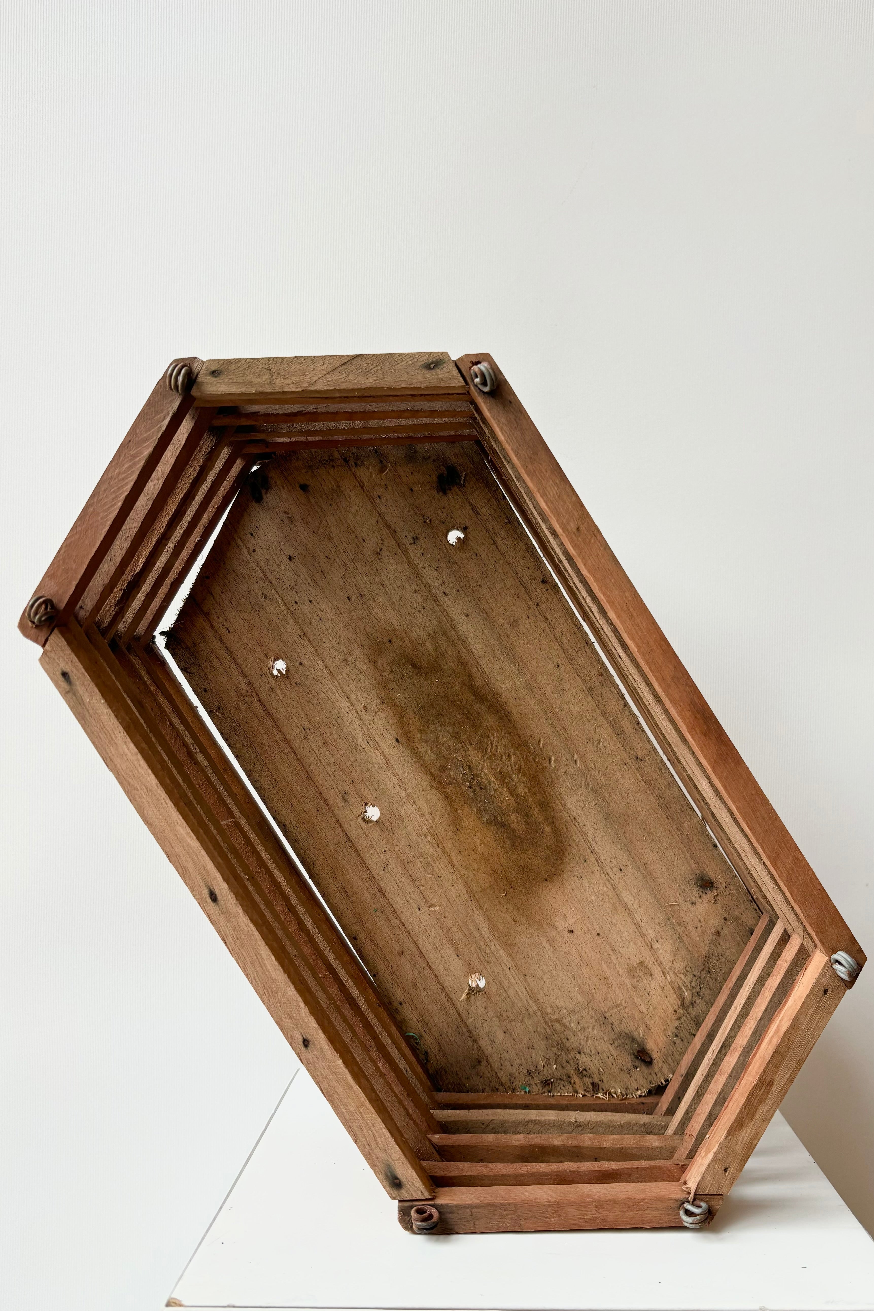 Interior view of elongated wooden hexagonal slatted basket with metal rings for string attachment, not included, against white background. 