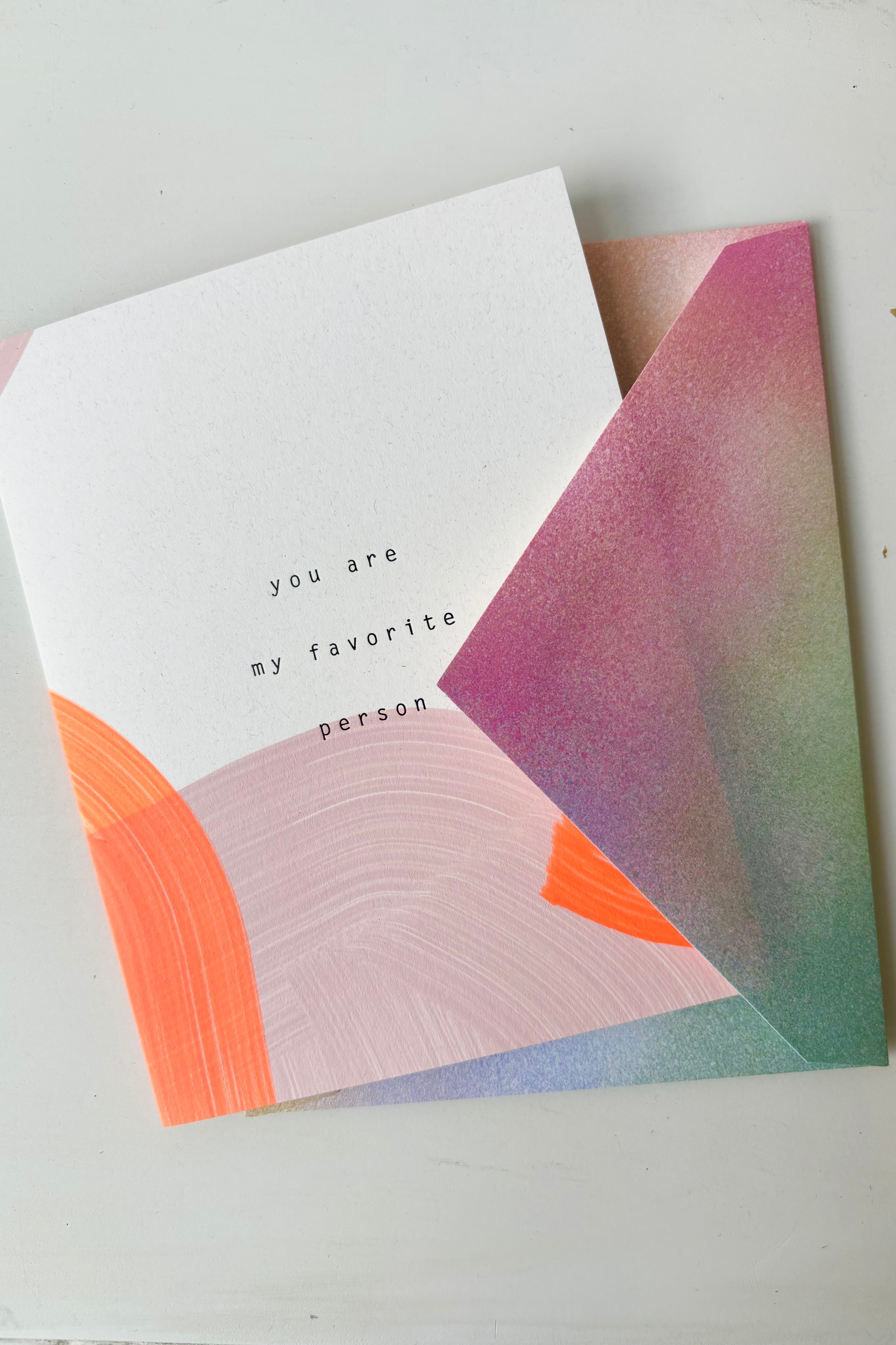 Hand painted greeting card with orange and pink abstract design and black lettering that says you are my favorite person displayed in multicolored envelope
