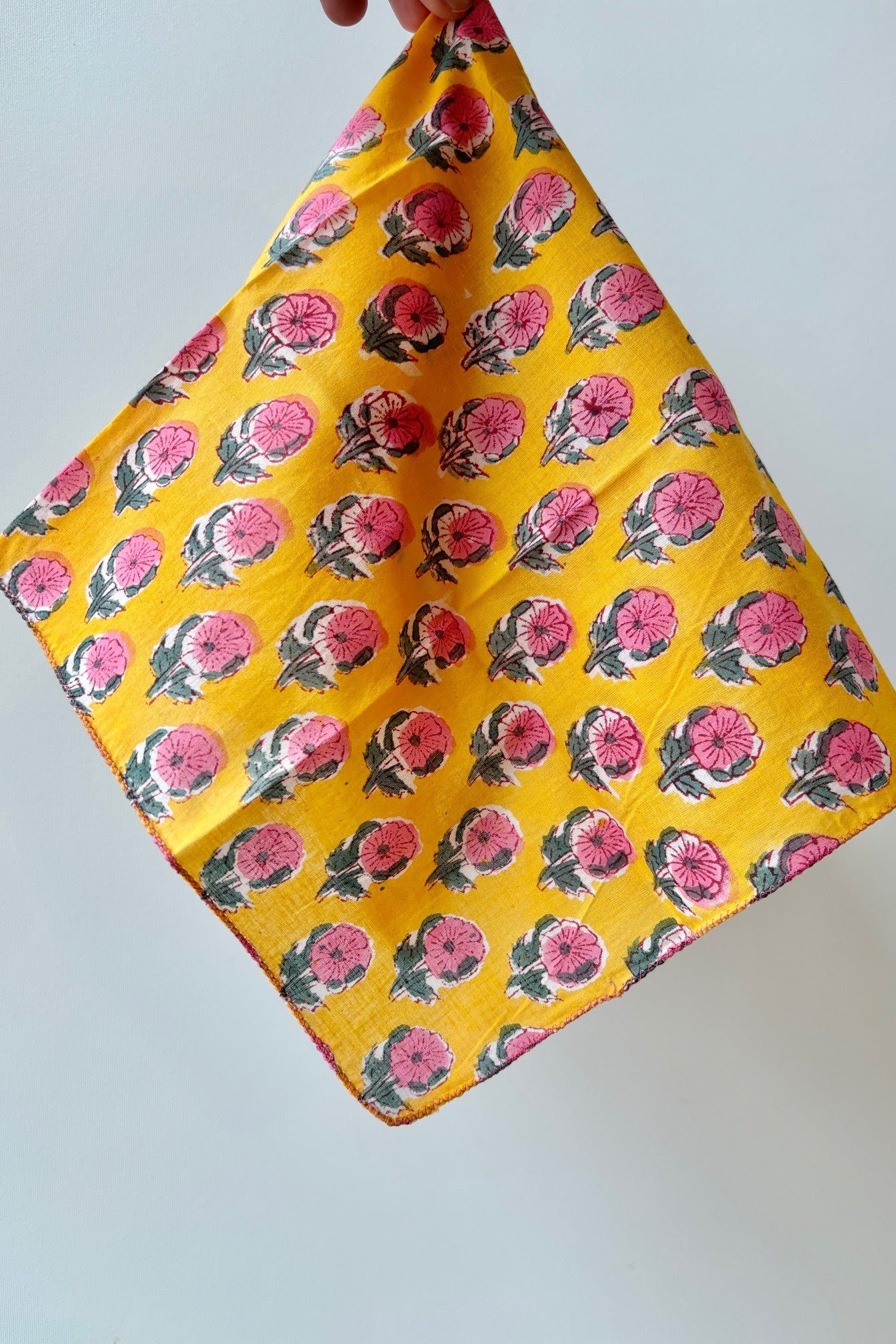 Handsewn napkin with pink and green flowers on a golden yellow background against white background