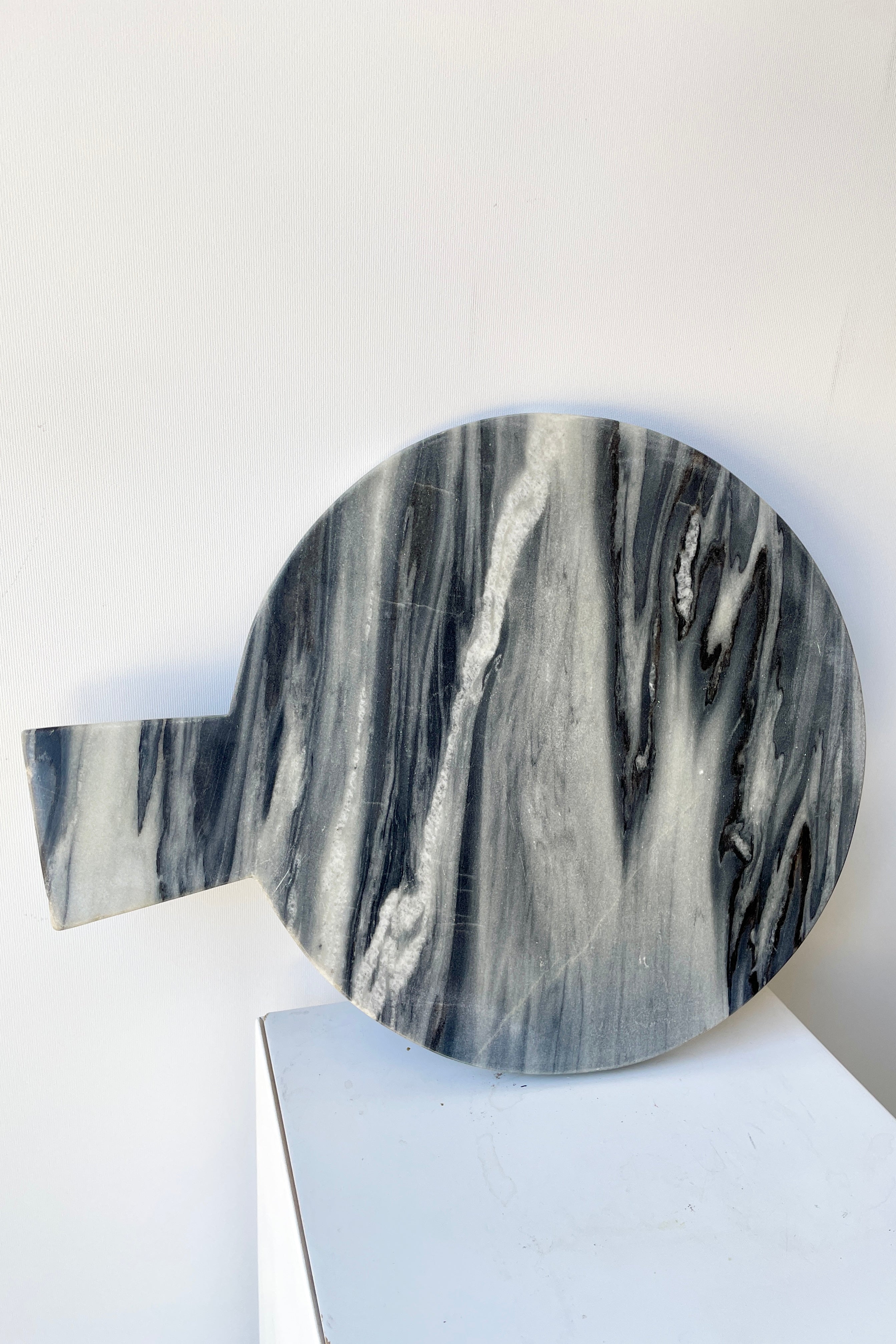 The black marble cheese board at Sprout-home leaning on its side against a white wall. 
