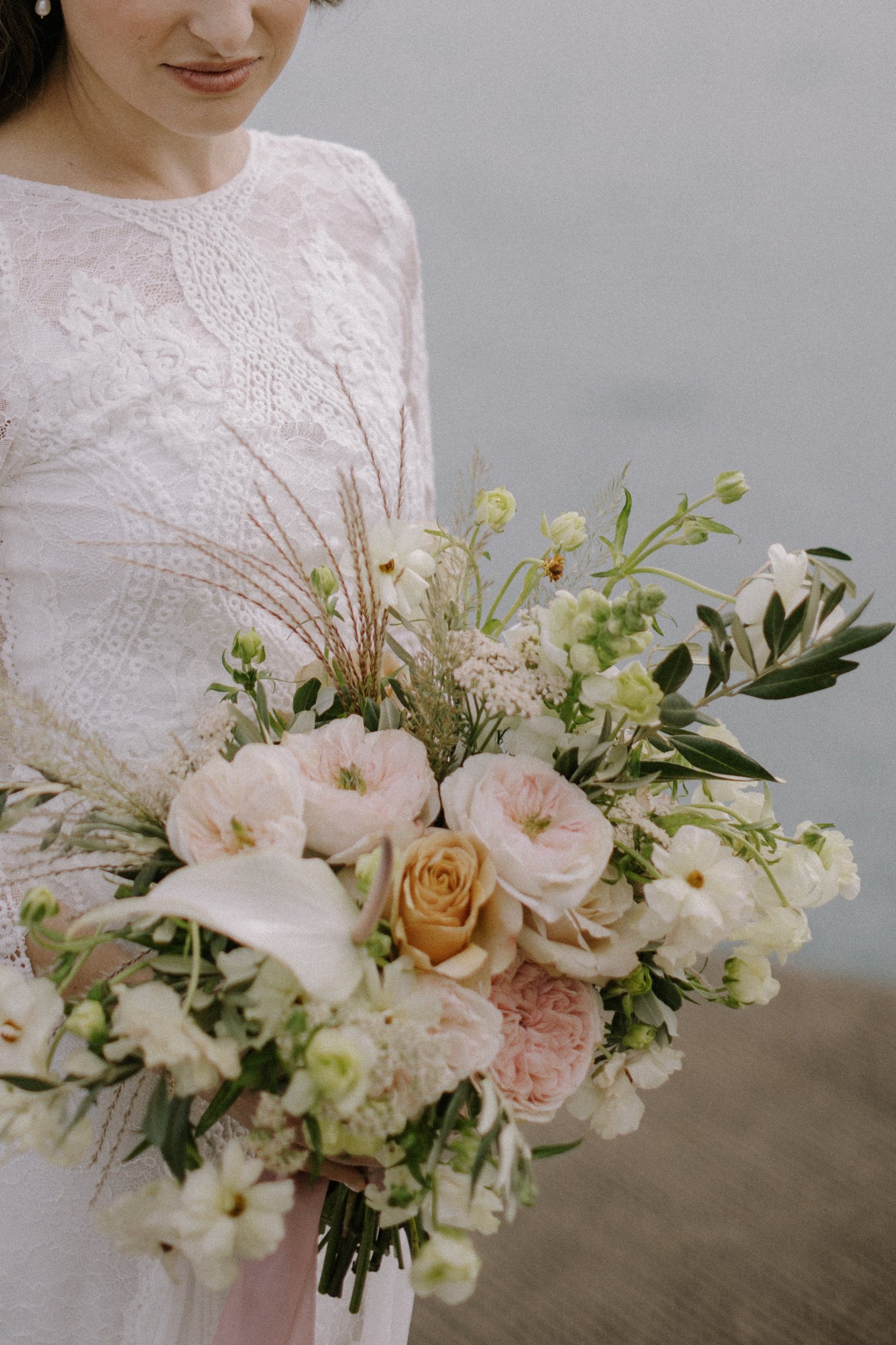 Kroster wedding with the bride in lace, holding a white and light pastel floral with hints of grass plumes.  arrangement by Sprout-home . Photograph by Samantha Elizabeth Creative