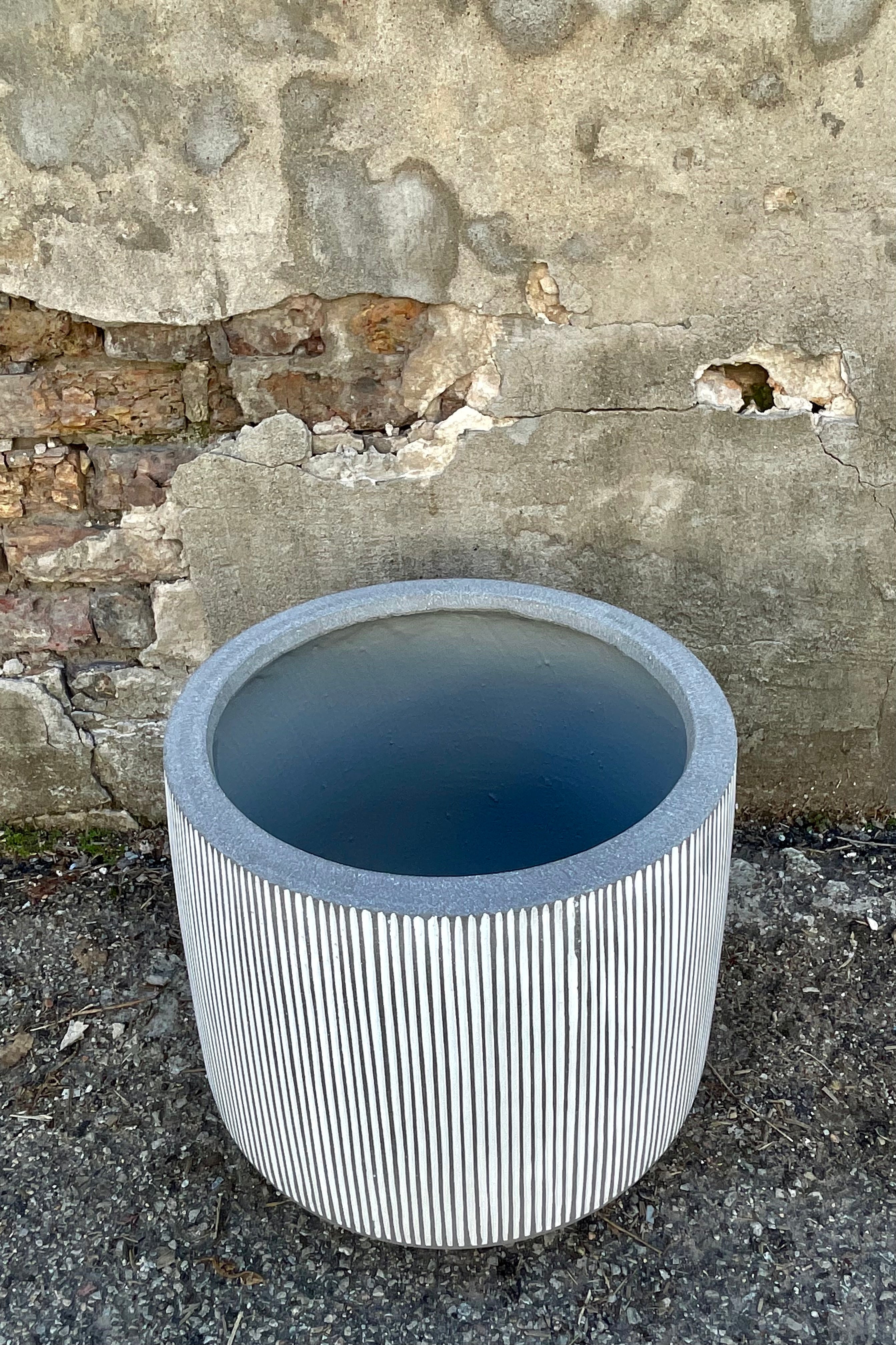 Photo from above of white and gray striped Harith pot against a cement wall.