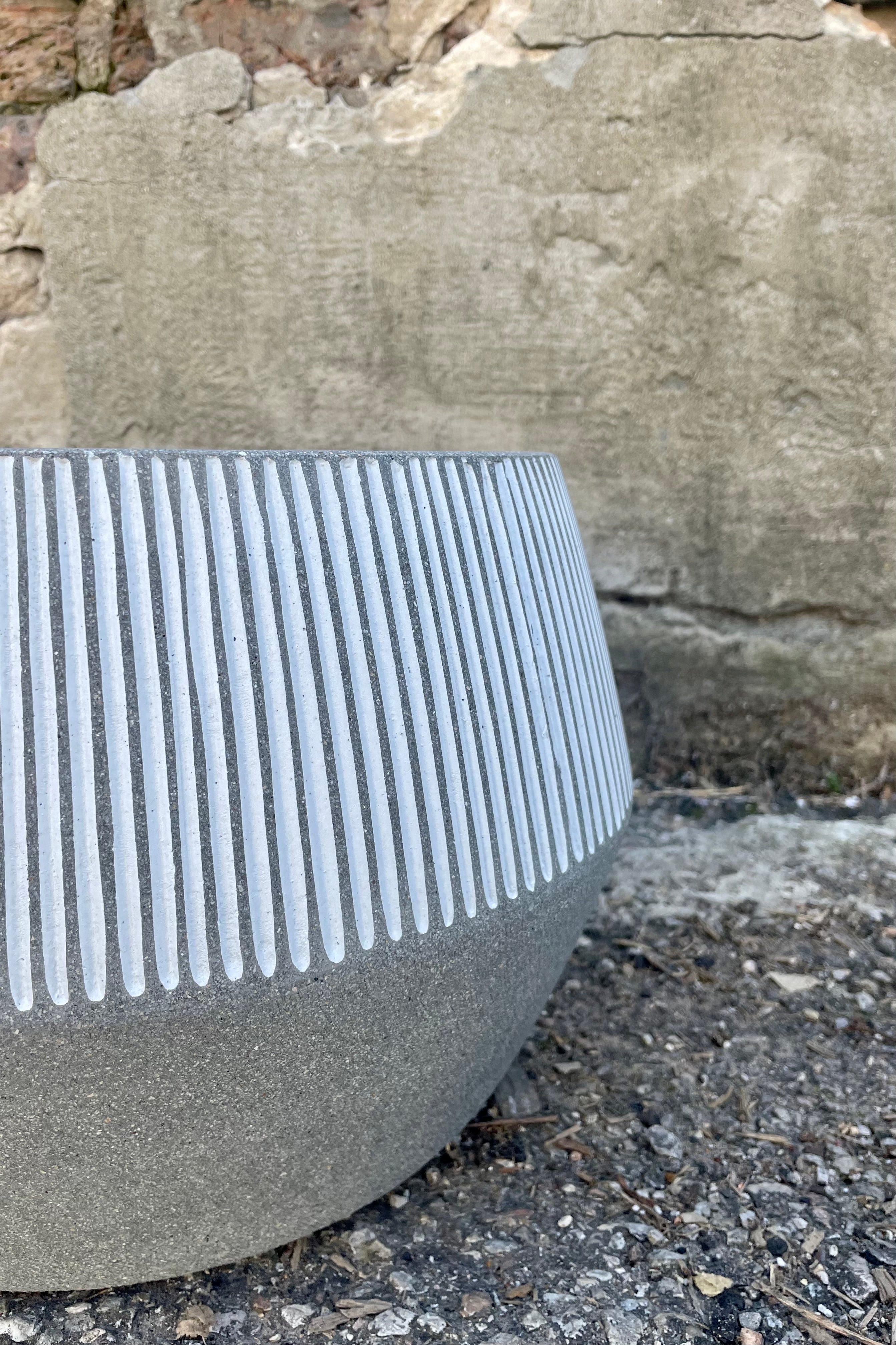 Photo of the angled side of a gray and white striped Harley Low Pot against a cement wall. 