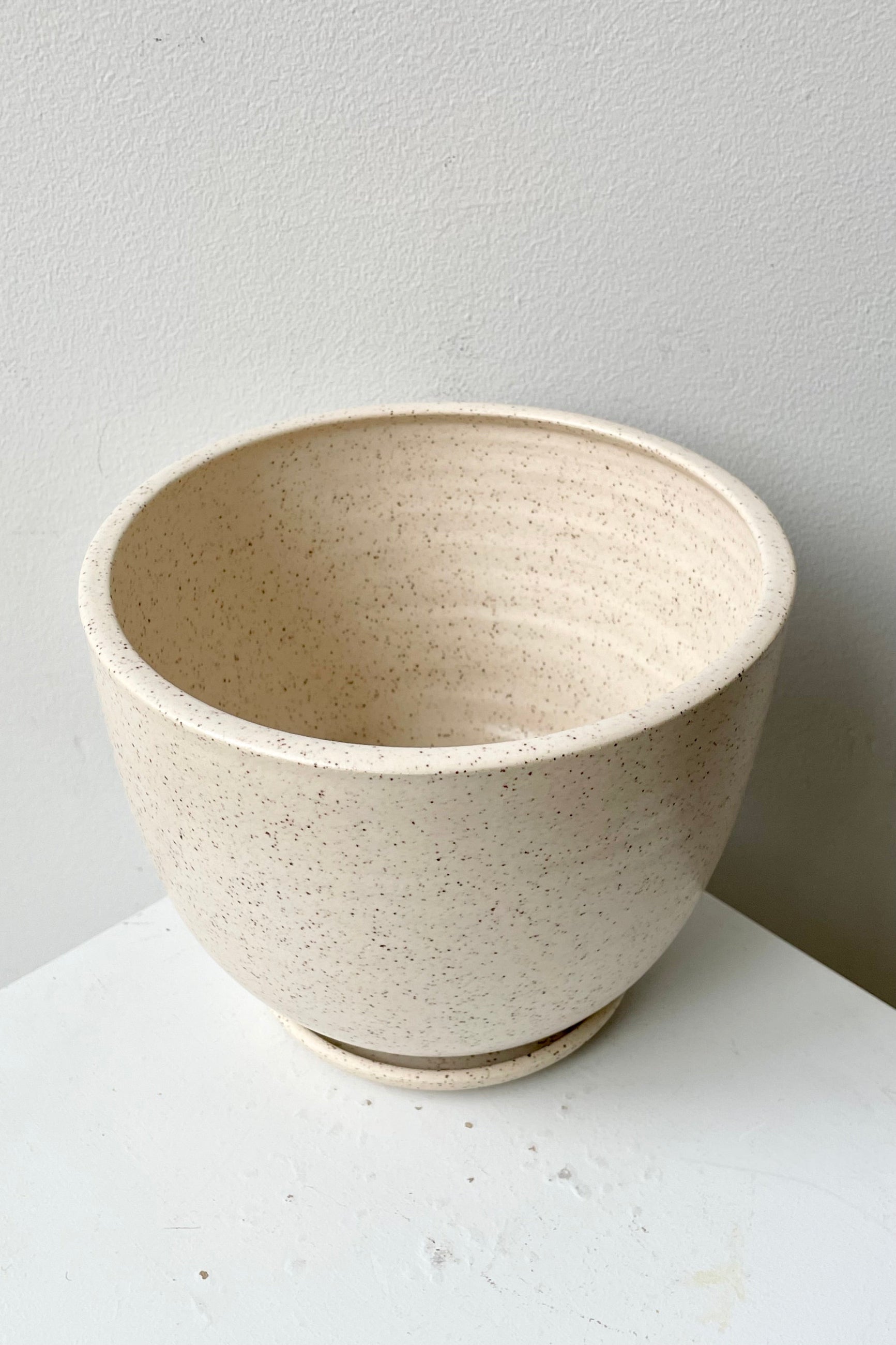 a view from above and side of the tabletop planter and saucer in the cream speckle finish. 