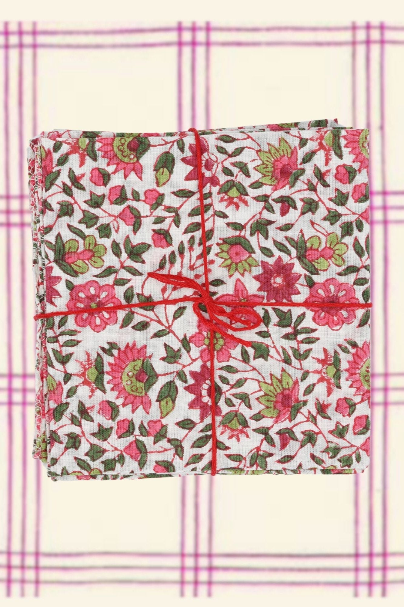 Cotton Napkins Chicorée Peonie by Suzette folded and tied with a red string on a pink and cream plaid background.