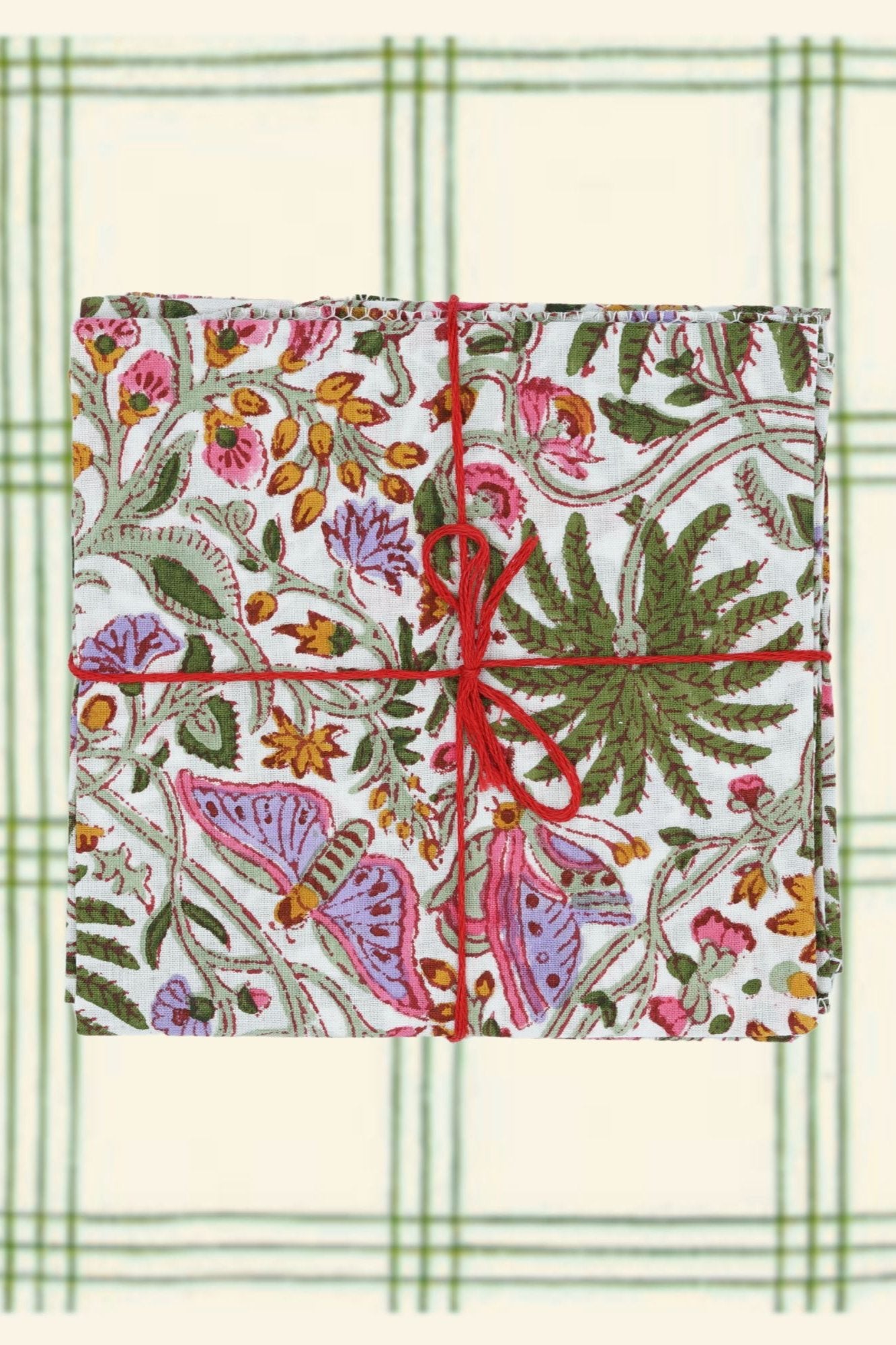 Suzette Cotton Napkins Primavera Cyprès folded, sitting on a green and cream plaid print and tied with a red string. 