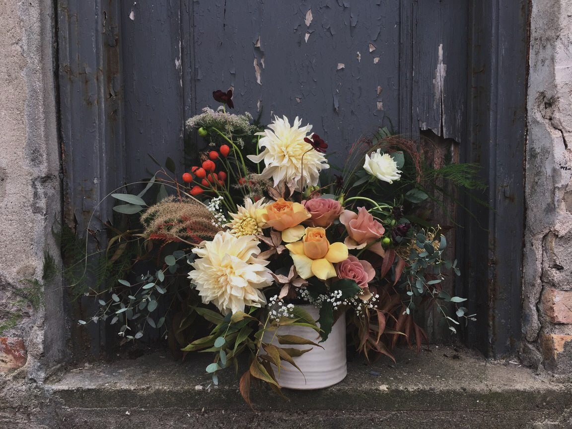 A soft and inviting fall arrangement by Sprout-home featuring fluffy white dahlia in front of a gray door. Photo by Sprout-home. 