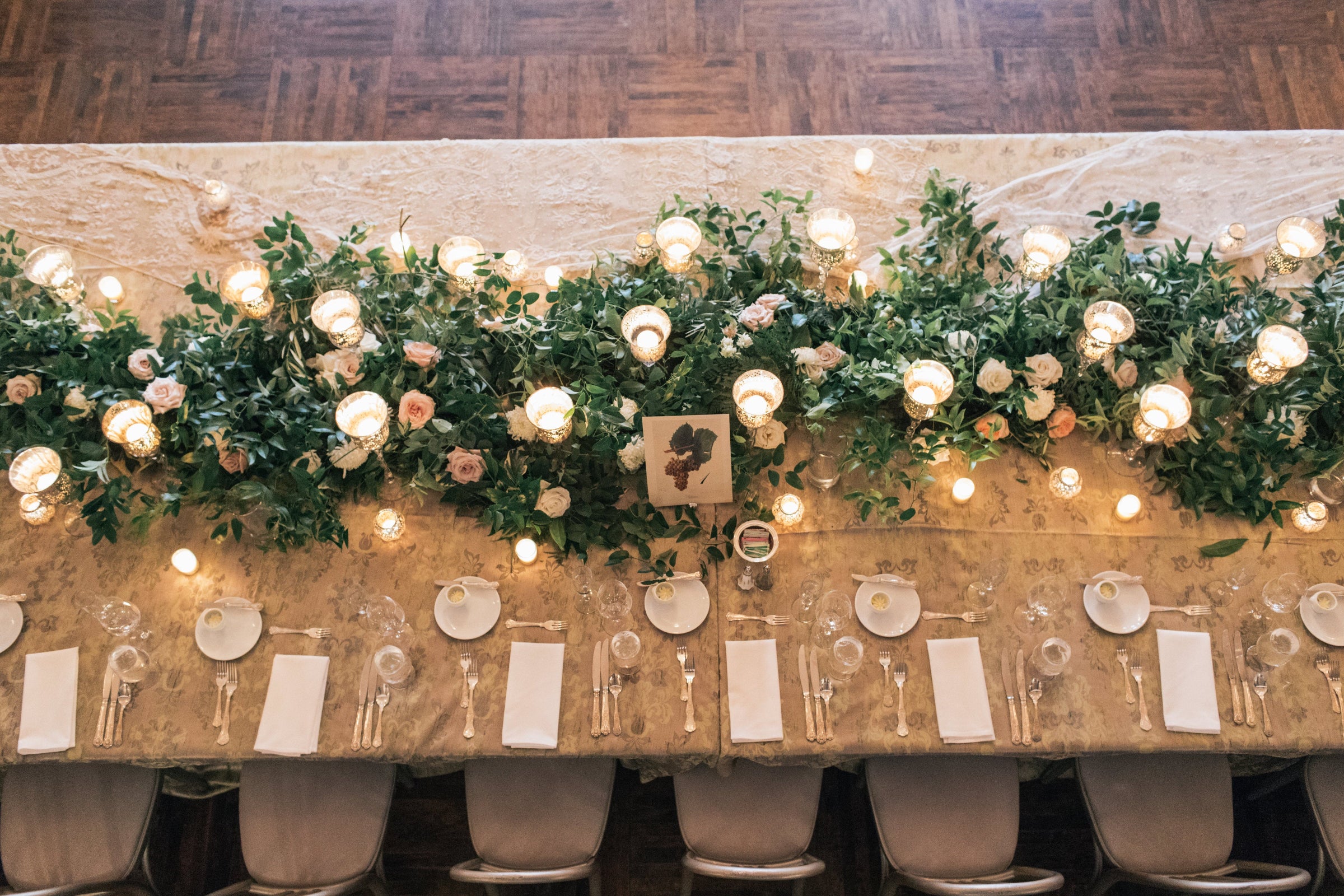 green wedding garland with white and pink floral and candles stretching down a table from above.  Photograph by Shannon Olesiak Photo