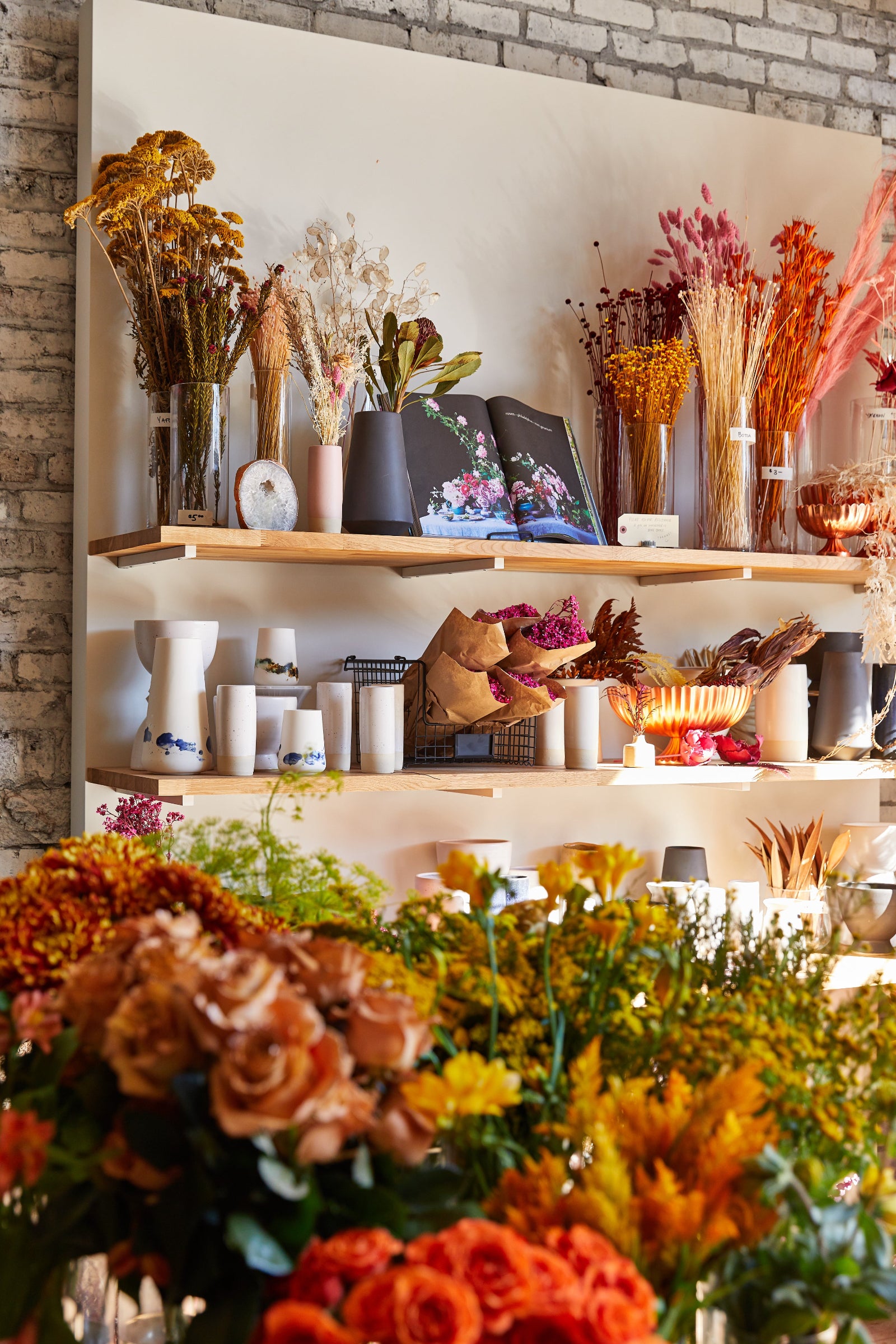 Display shelves es at Sprout-home floral with warm colored dried floral and vases and fresh floral in the foreground.