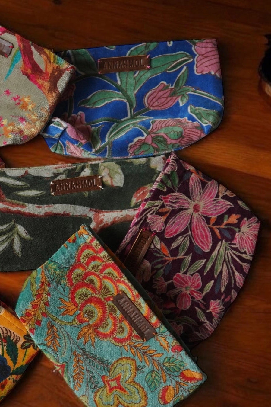 Collection of colorful fabric pouches with floral patterns on a wooden surface ©Annahmol