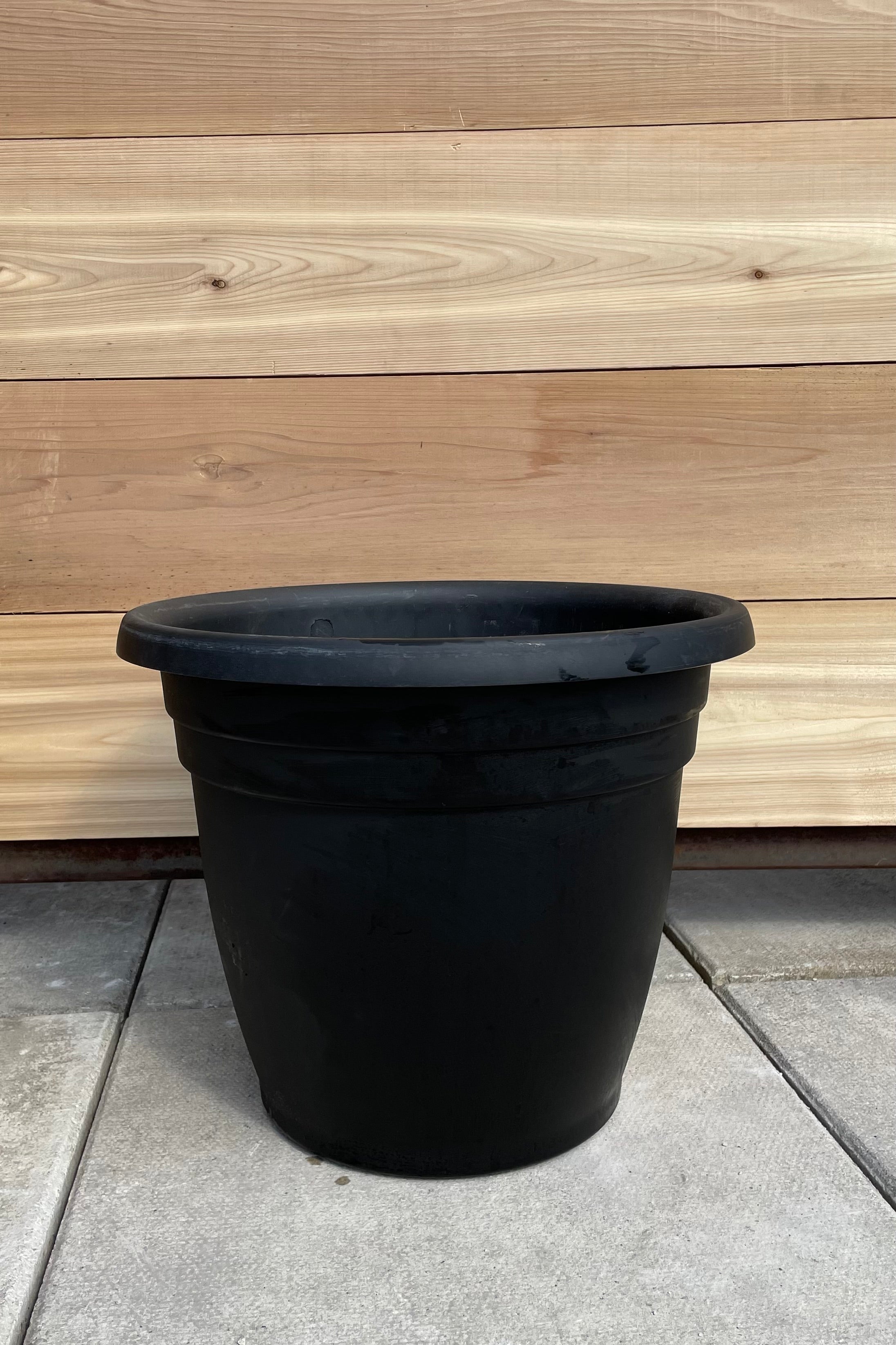 The black 16" round Emma planter against a cedar wall. 