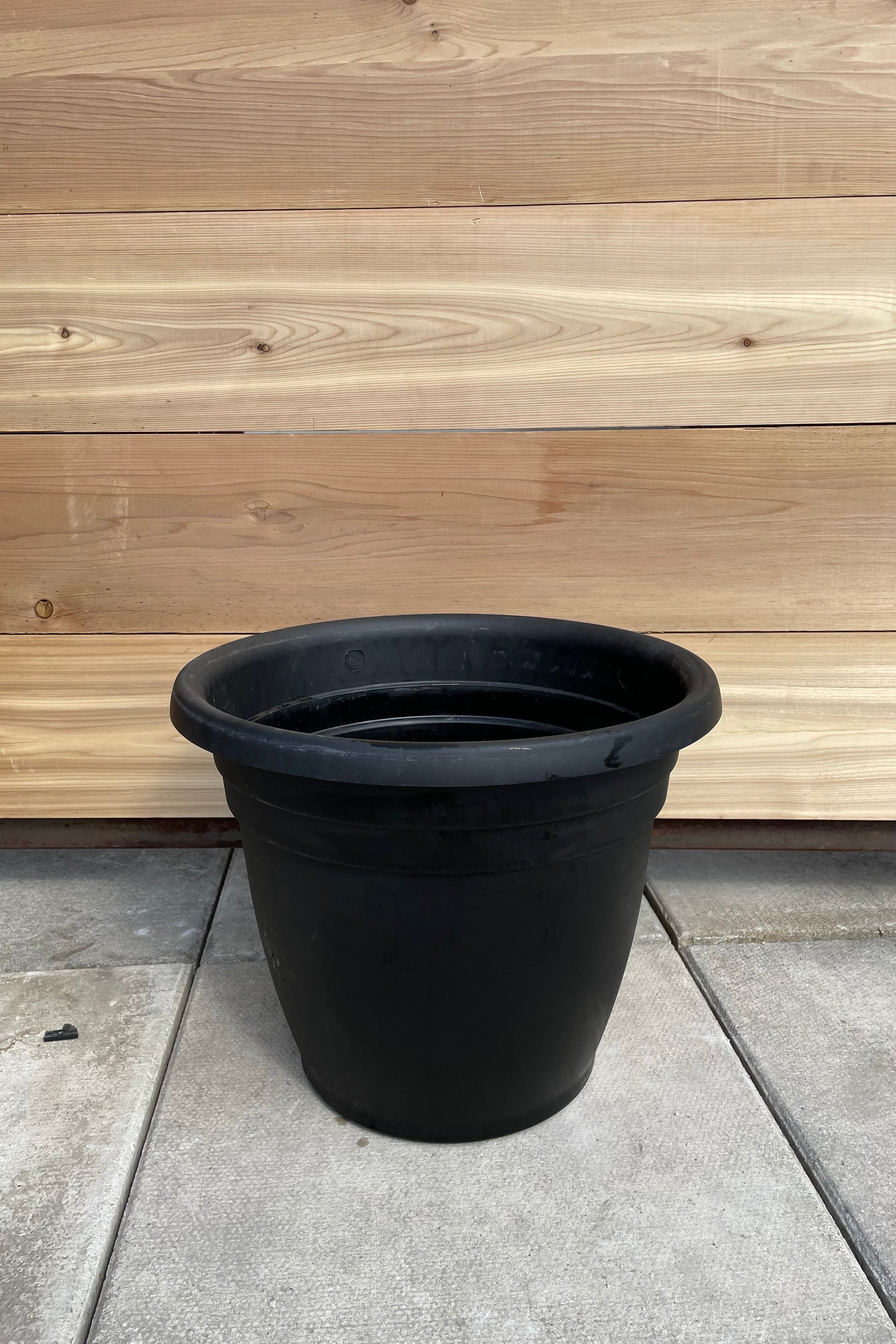 The black 16" round Emma planter against a cedar wall. 