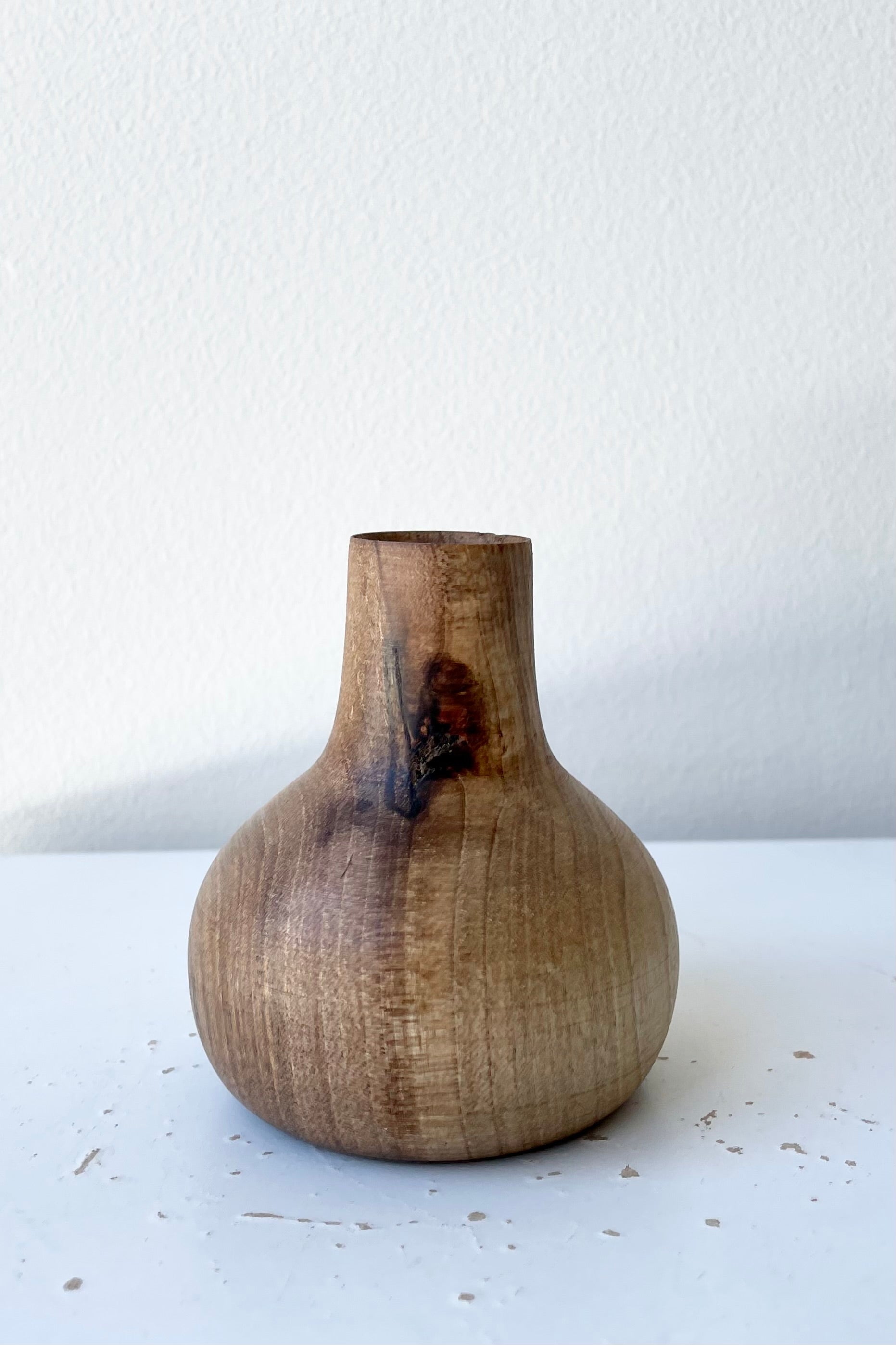 The walnut Nina wood vase against a white wall at Sprout-home.