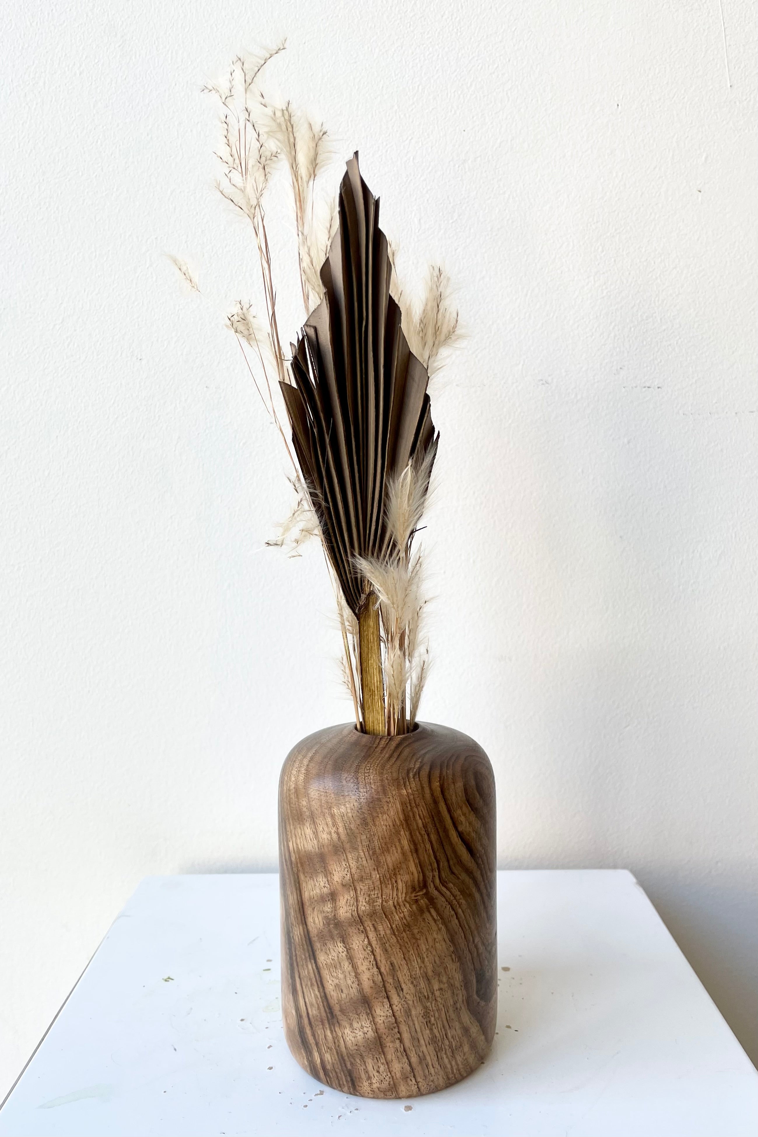 Patti walnut wood vase medium size with dried floral against a white wall at Sprout-home. 