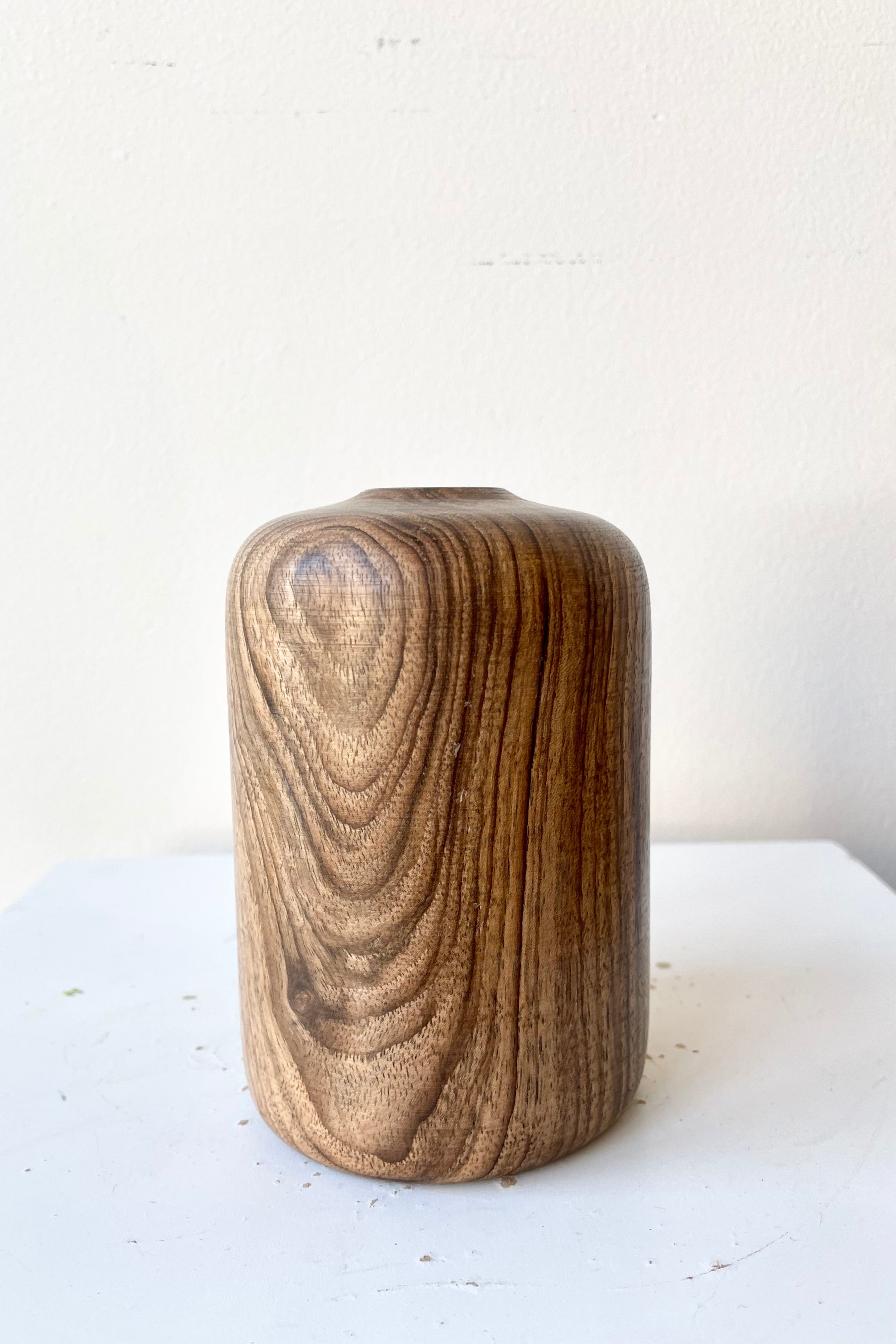 Patti walnut wood vase medium size against a white wall at Sprout-home. 