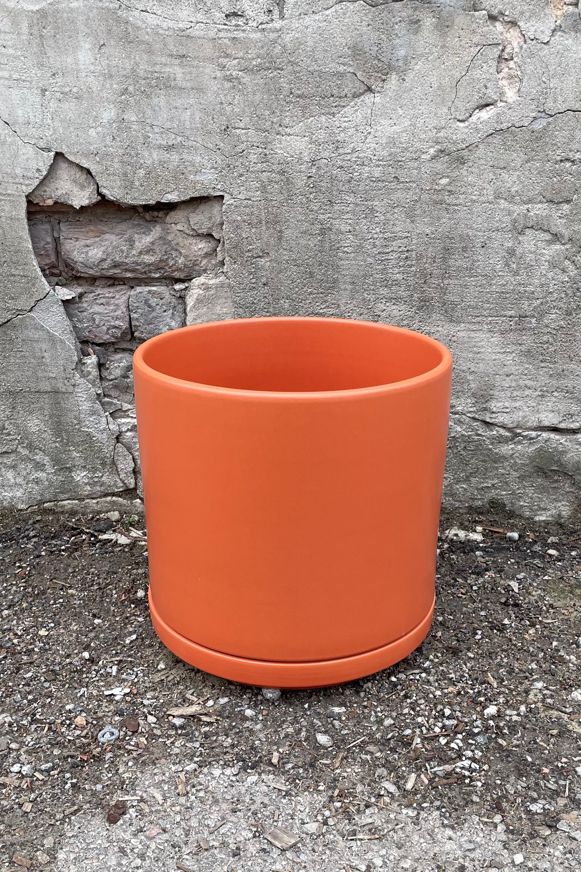 10" rust solid cylinder and saucer against a cement wall. 