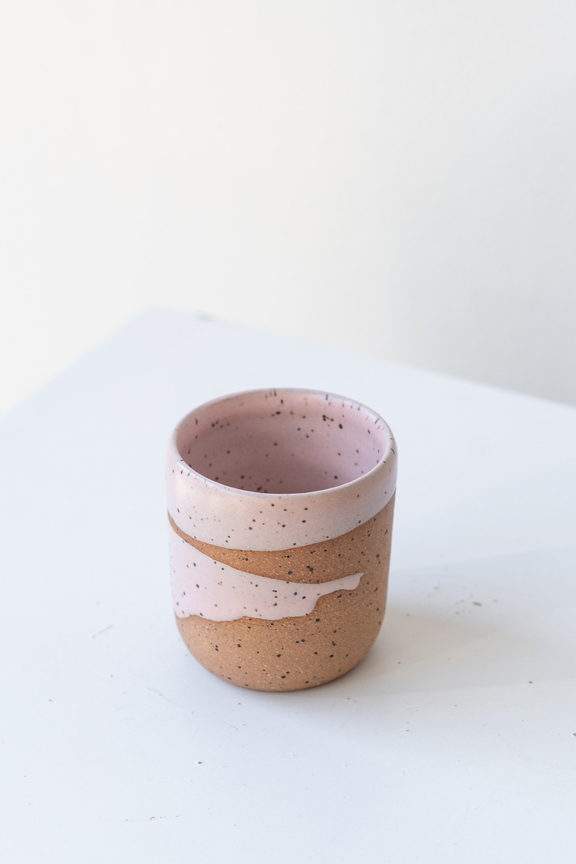 Pink Coastal Glaze Cup by Christina Kosinski sits on a white surface in a white room