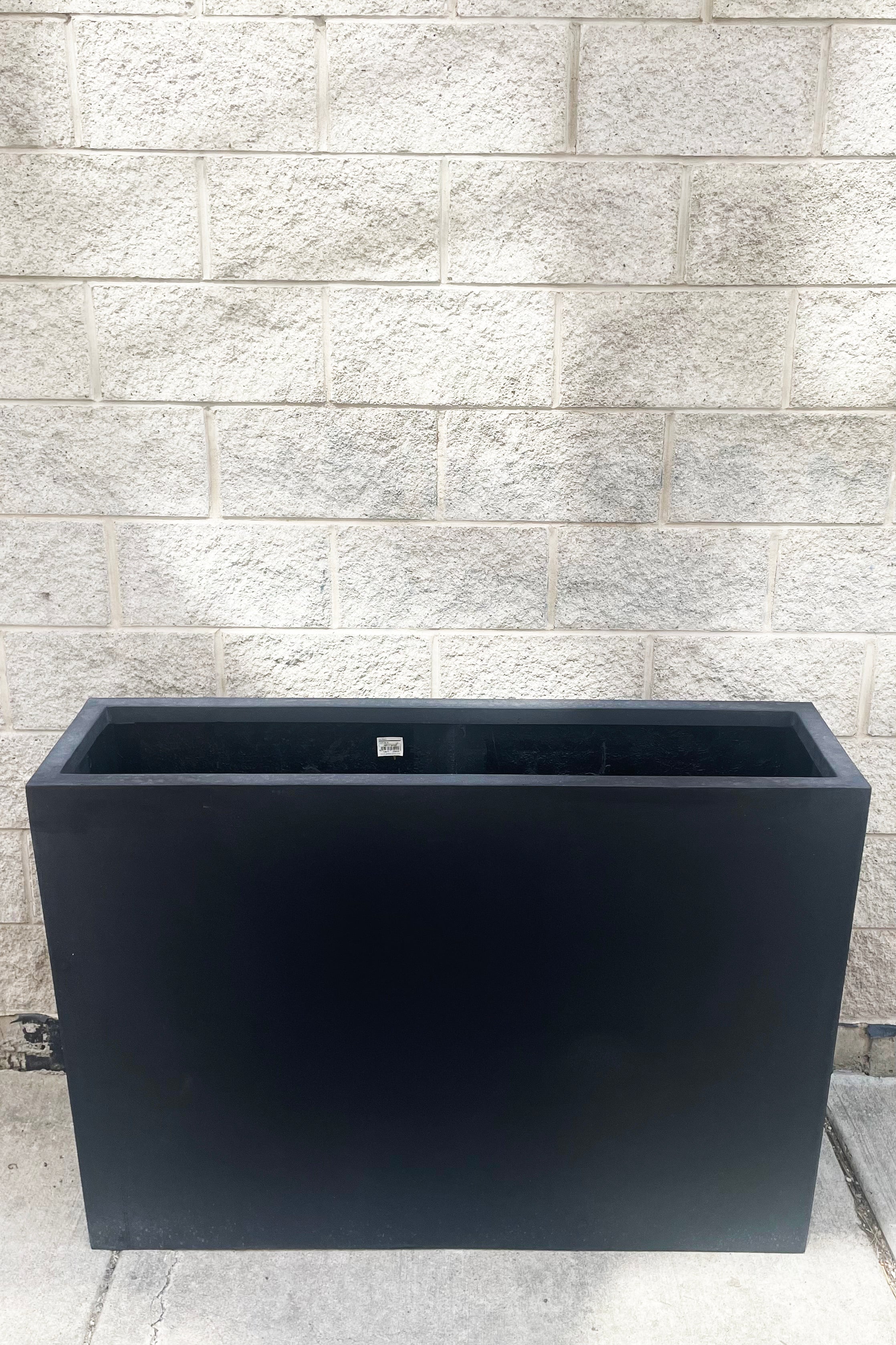 A slight overhead view of Jort Slim Fiberstone Planter black large against concrete backdrop