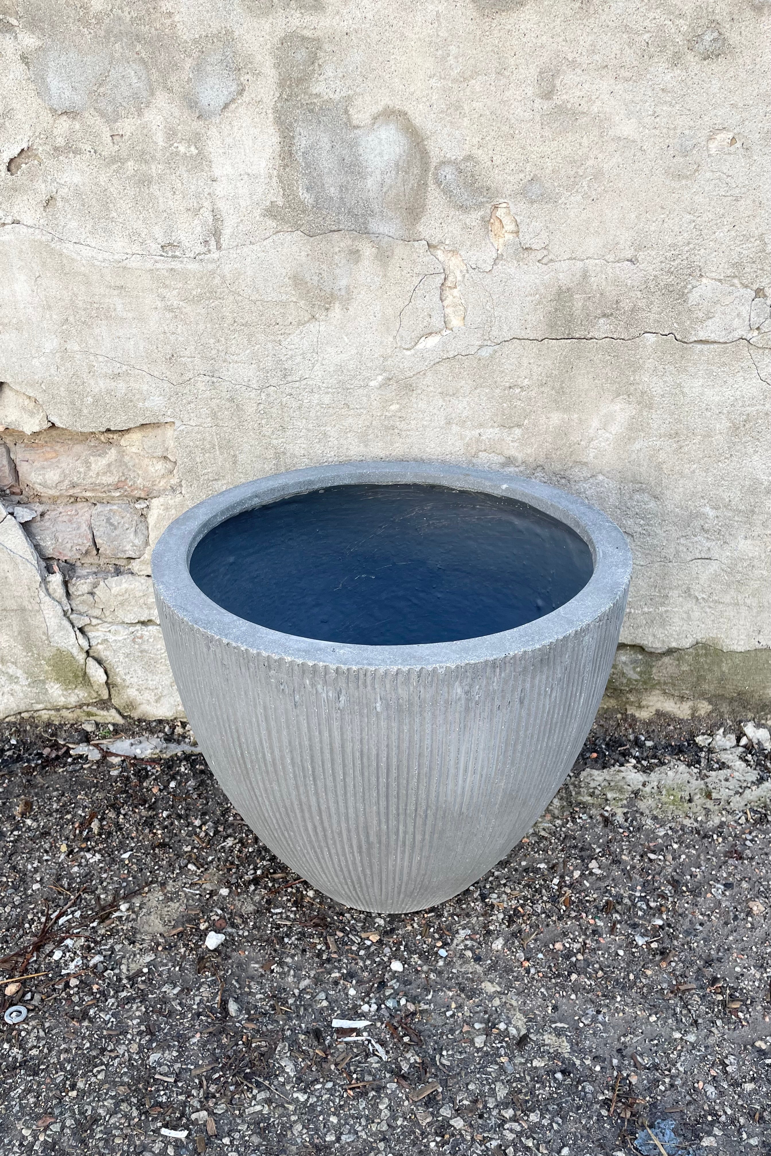 The dark grey extra small Jesslyn Pot with vertical ridges against a concrete wall at Sprout-home.