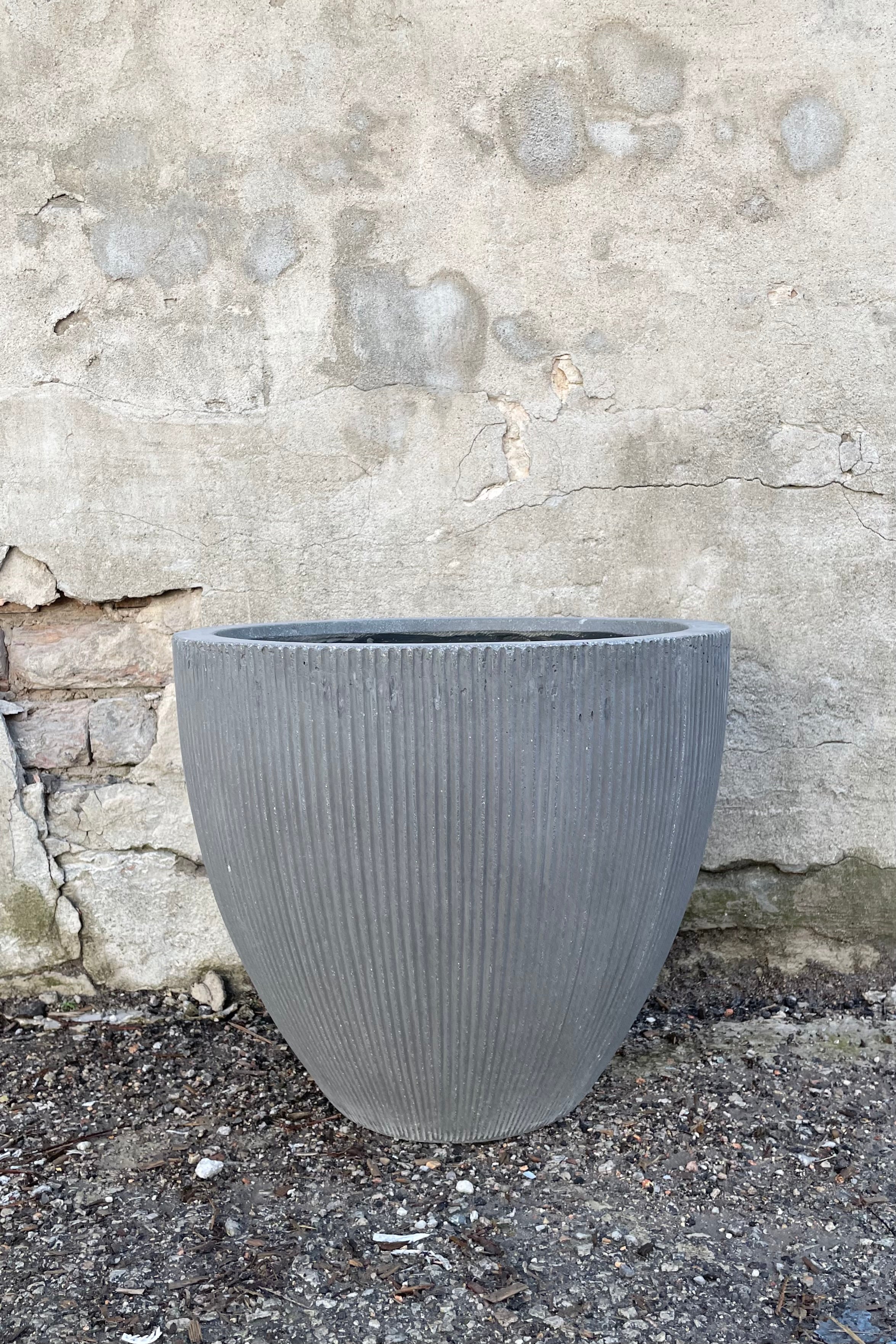 The dark grey extra small Jesslyn Pot with vertical ridges against a concrete wall at Sprout-home.
