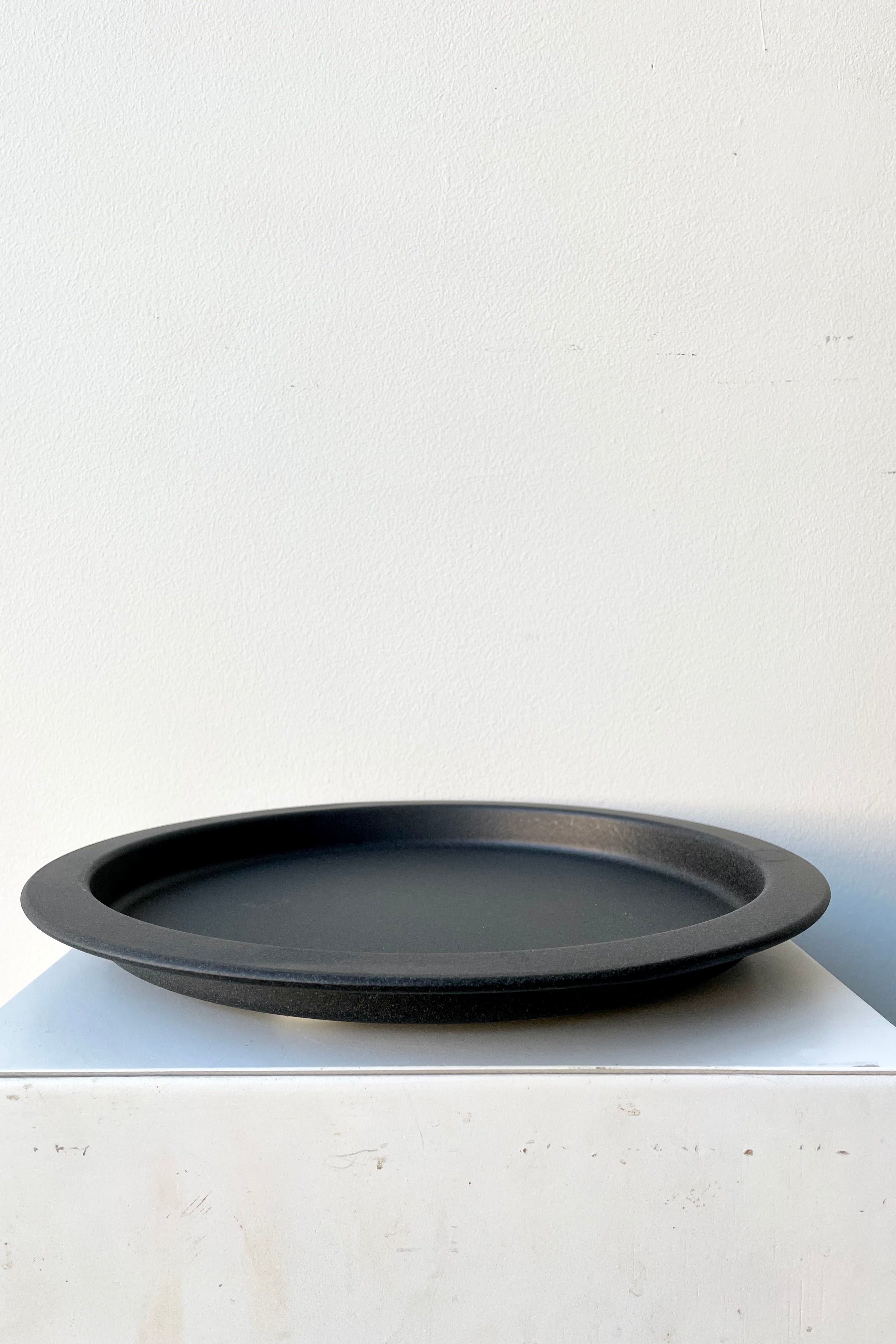 A speckled grey saucer against a while wall at Sprout-home. 