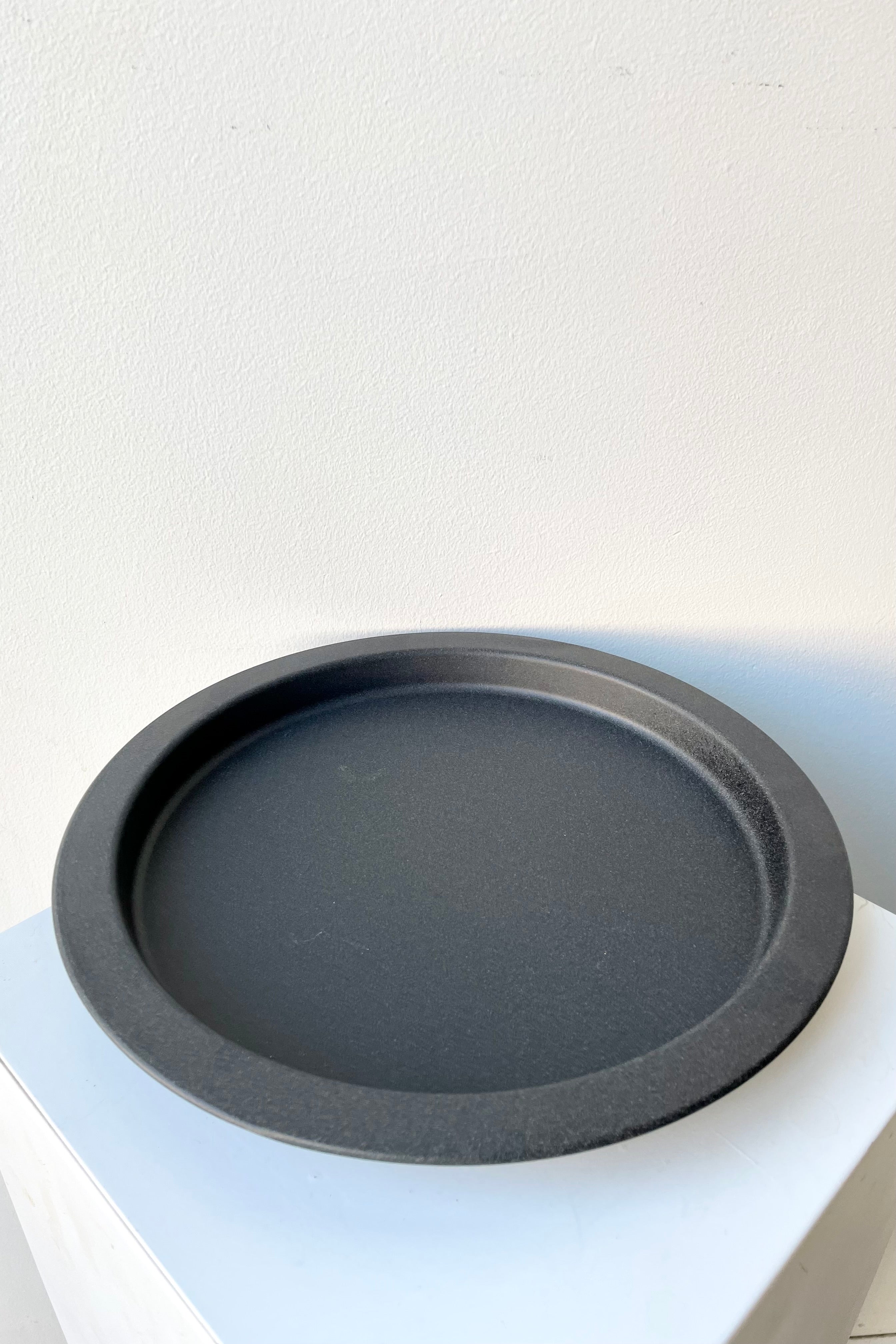 A speckled grey saucer against a while wall at Sprout-home. 