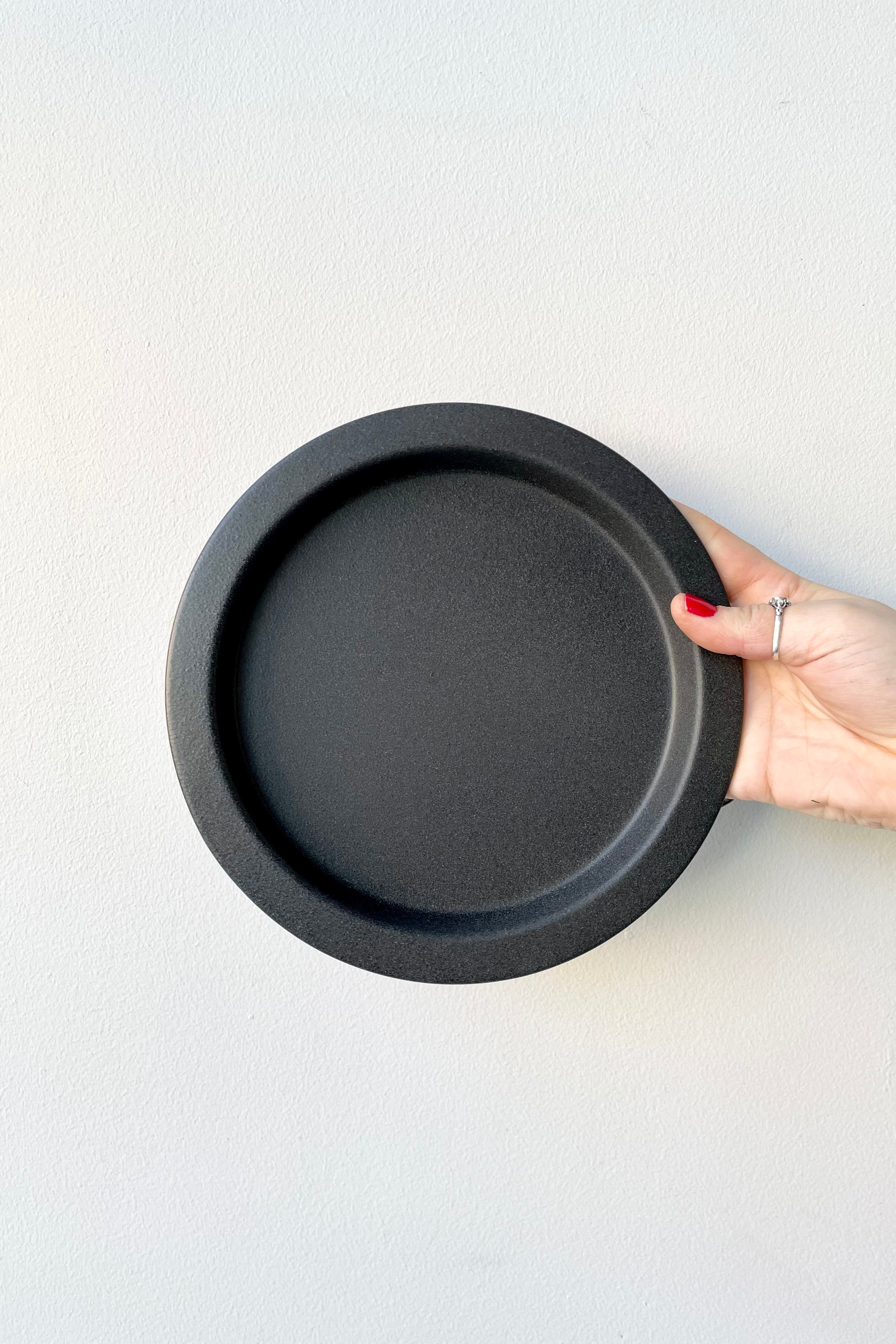 8" speckled grey saucer being held up against a white wall at Sprout-home. 